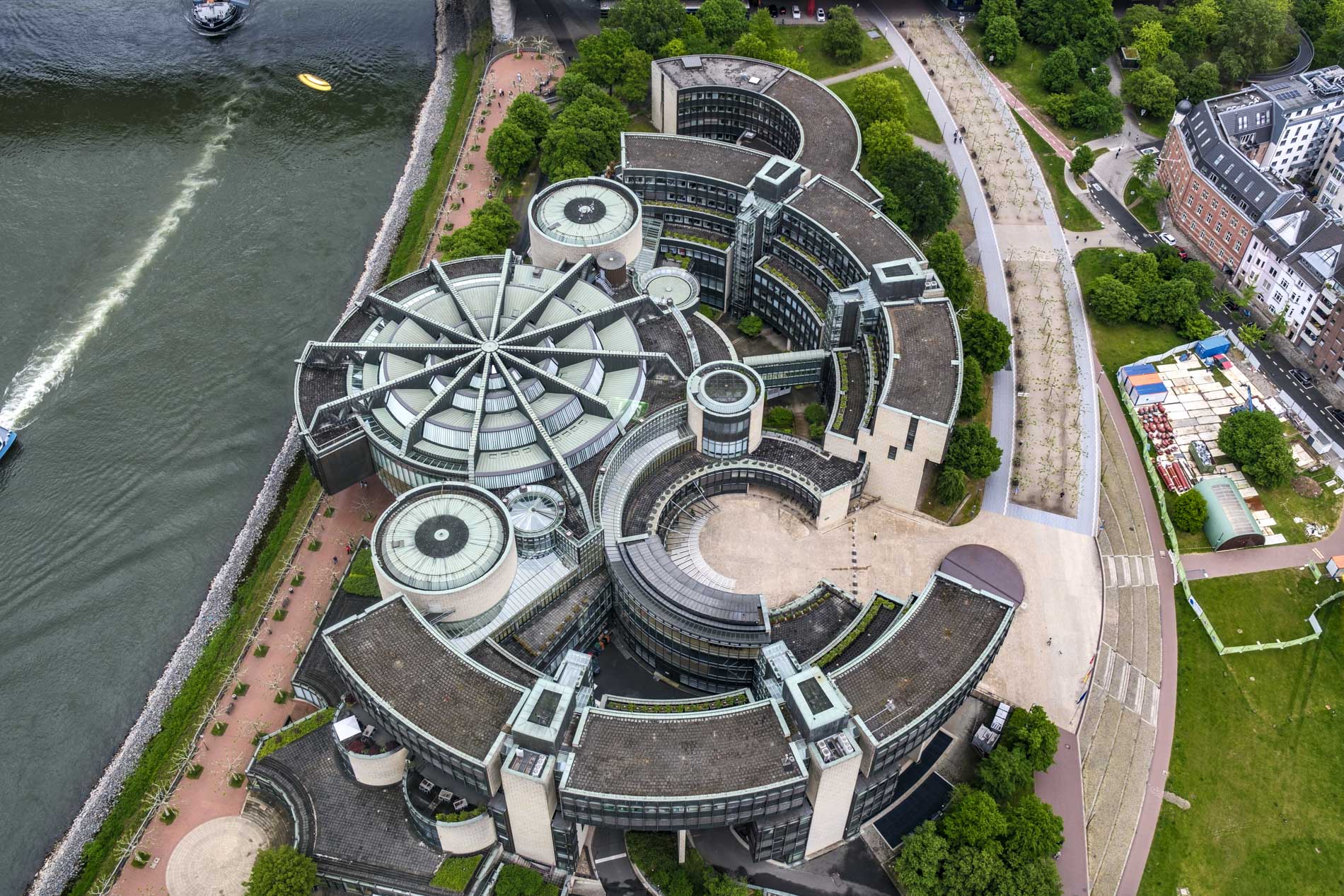 Aerial view of a modern architectural building with a circular design, surrounded by greenery and a river, showcasing its unique structure and layout.