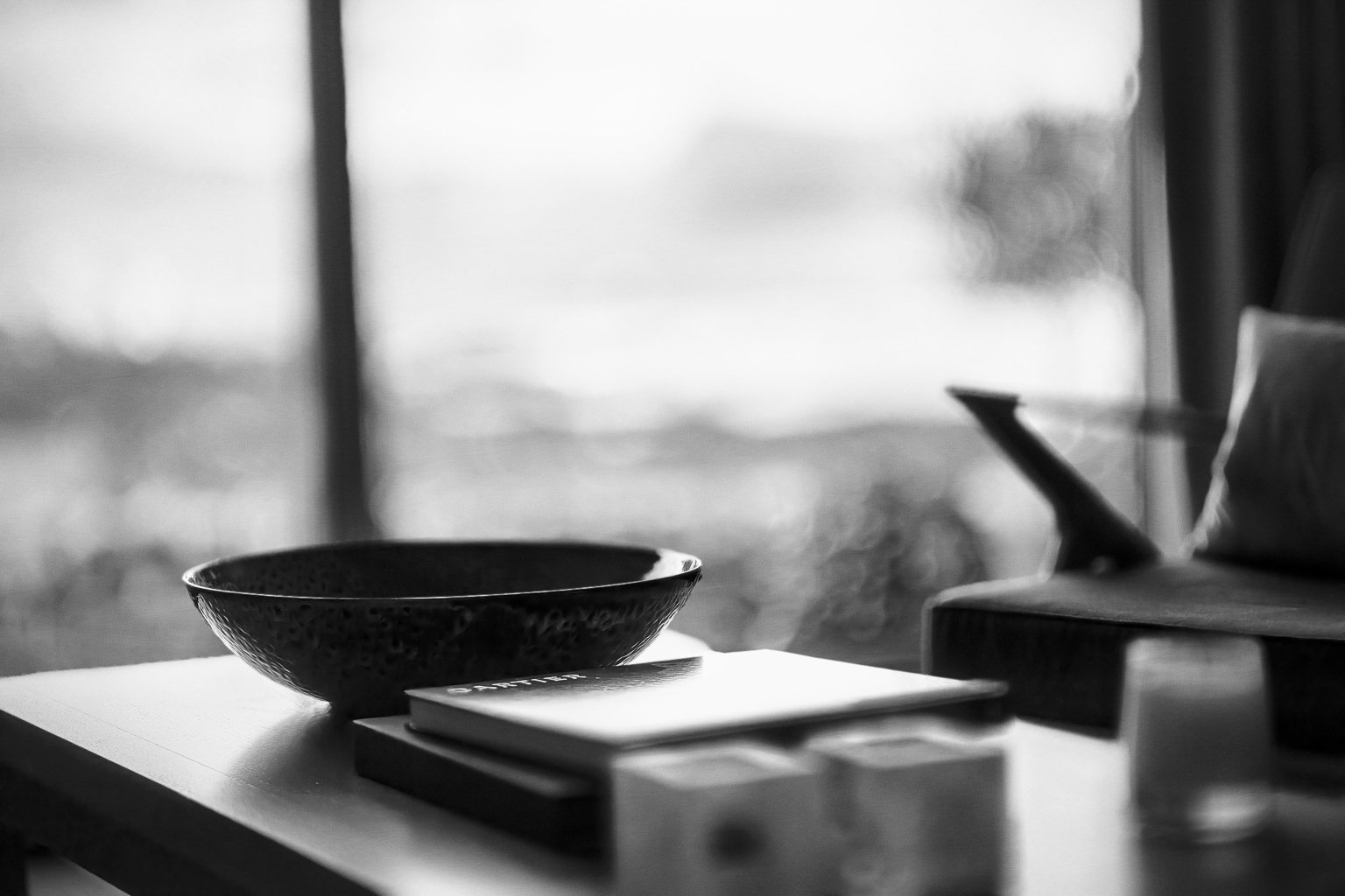 A black and white photo featuring a decorative bowl on a table, with books stacked nearby and a blurred background suggesting a cozy interior.