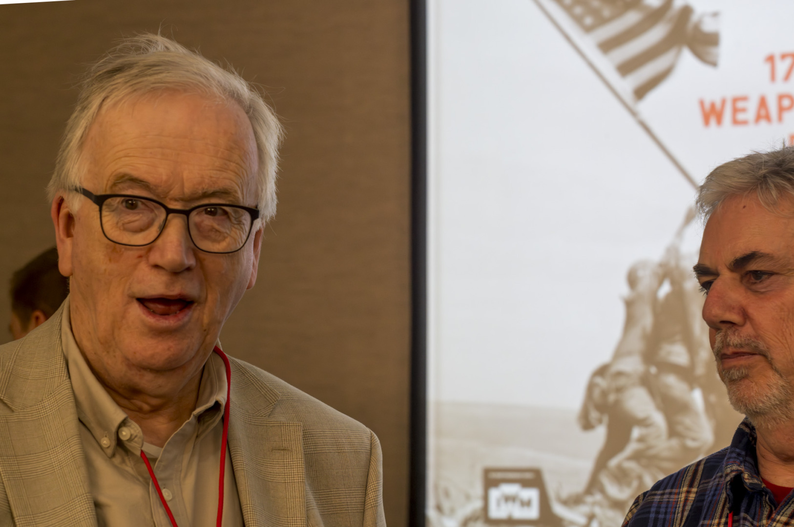 Two men standing in front of a presentation screen, one appearing surprised and the other looking serious.