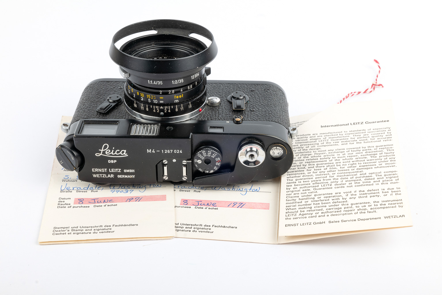 A vintage Leica M4 camera positioned on top of an open international warranty document, showcasing details such as the model number and company information.