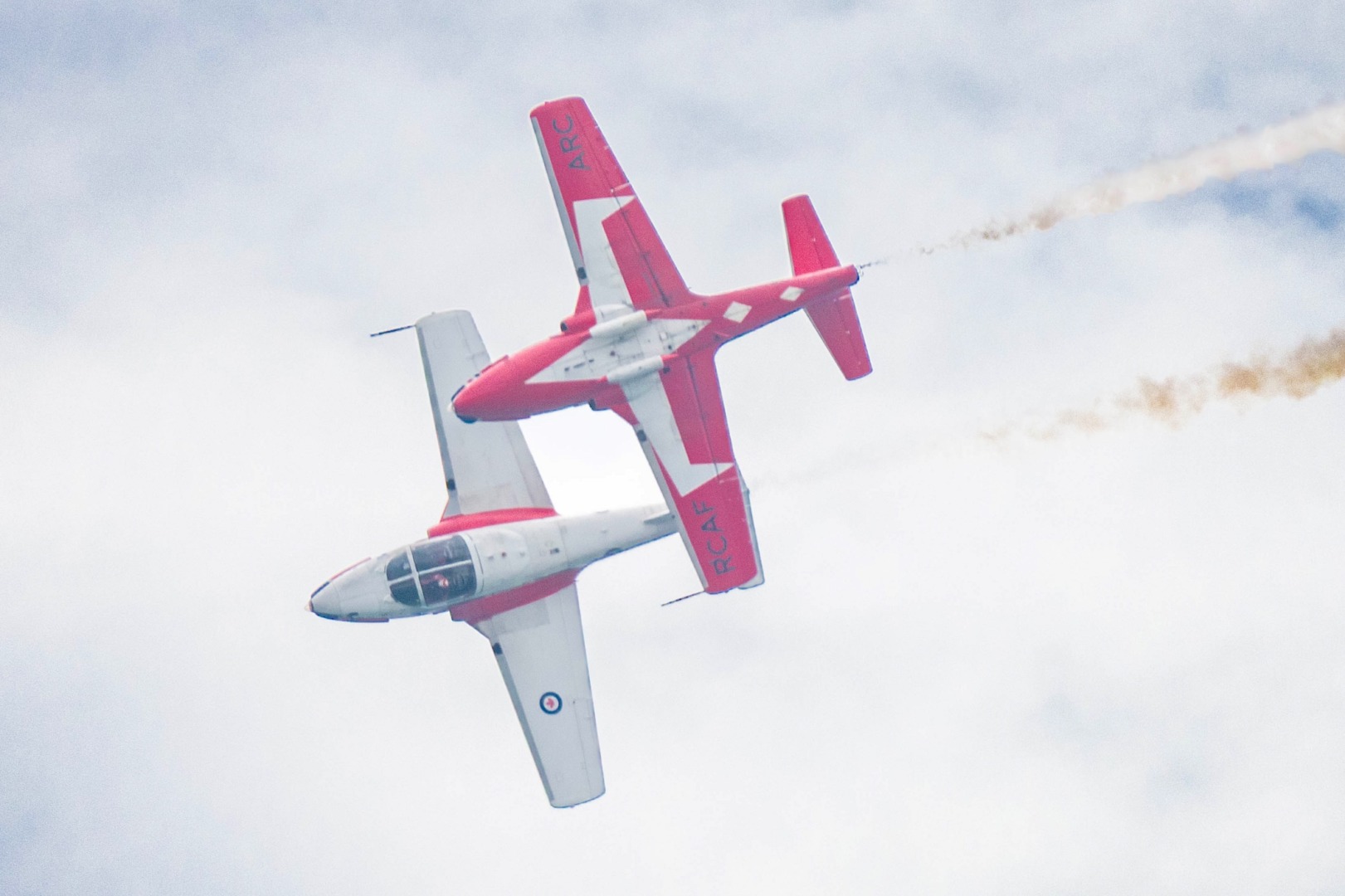 Two red and white jets flying in formation, trailing white smoke.