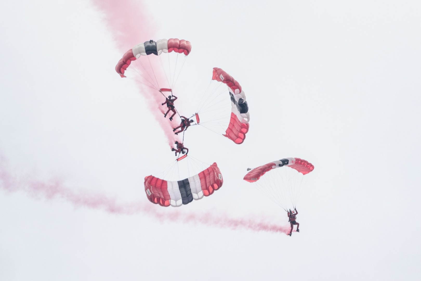 Four parachutists with red, white and blue parachutes in close formation, trailing red smoke.