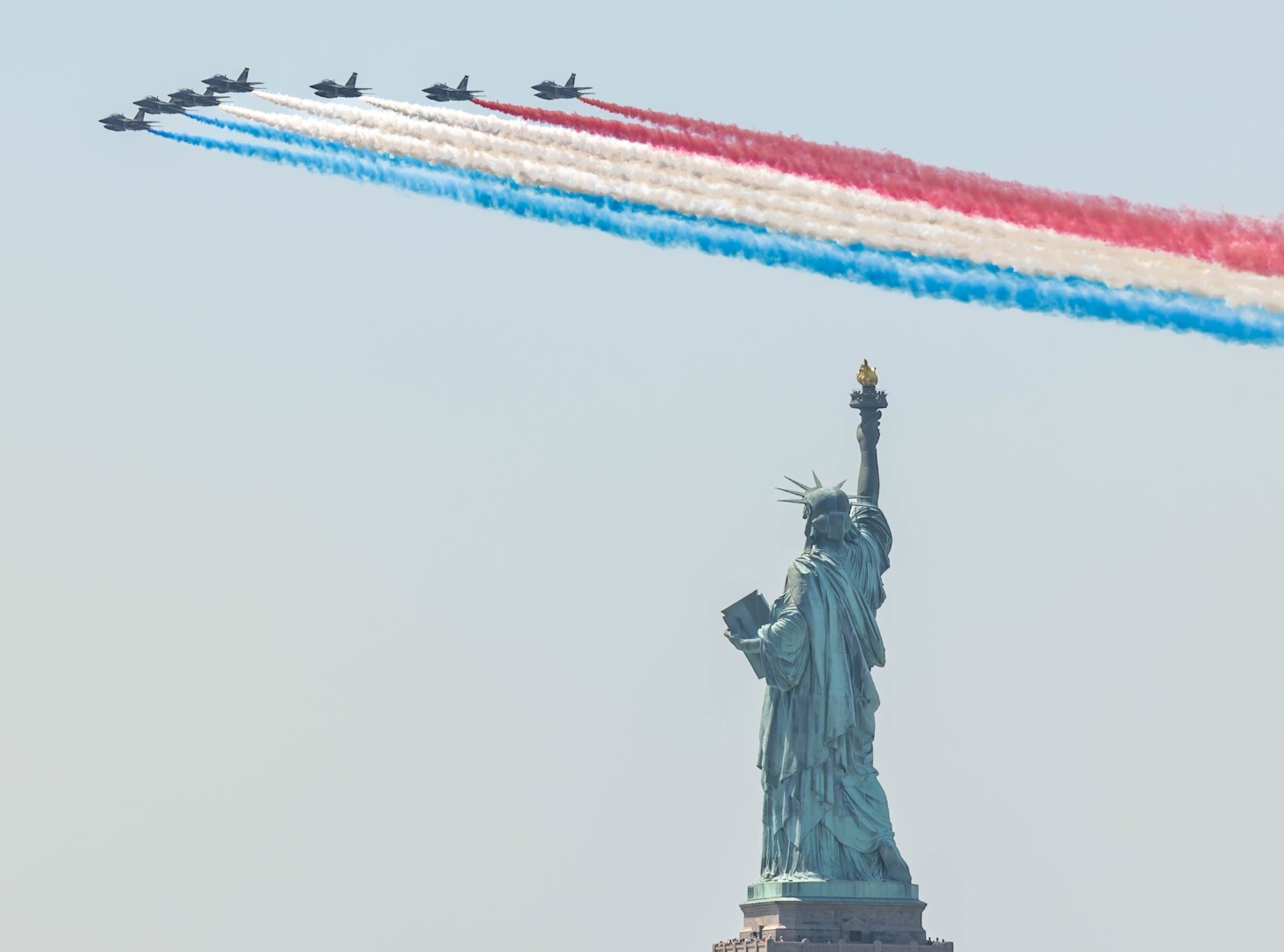 Jet display team trailing red, white and blue smoke over the Statue of Liberty.