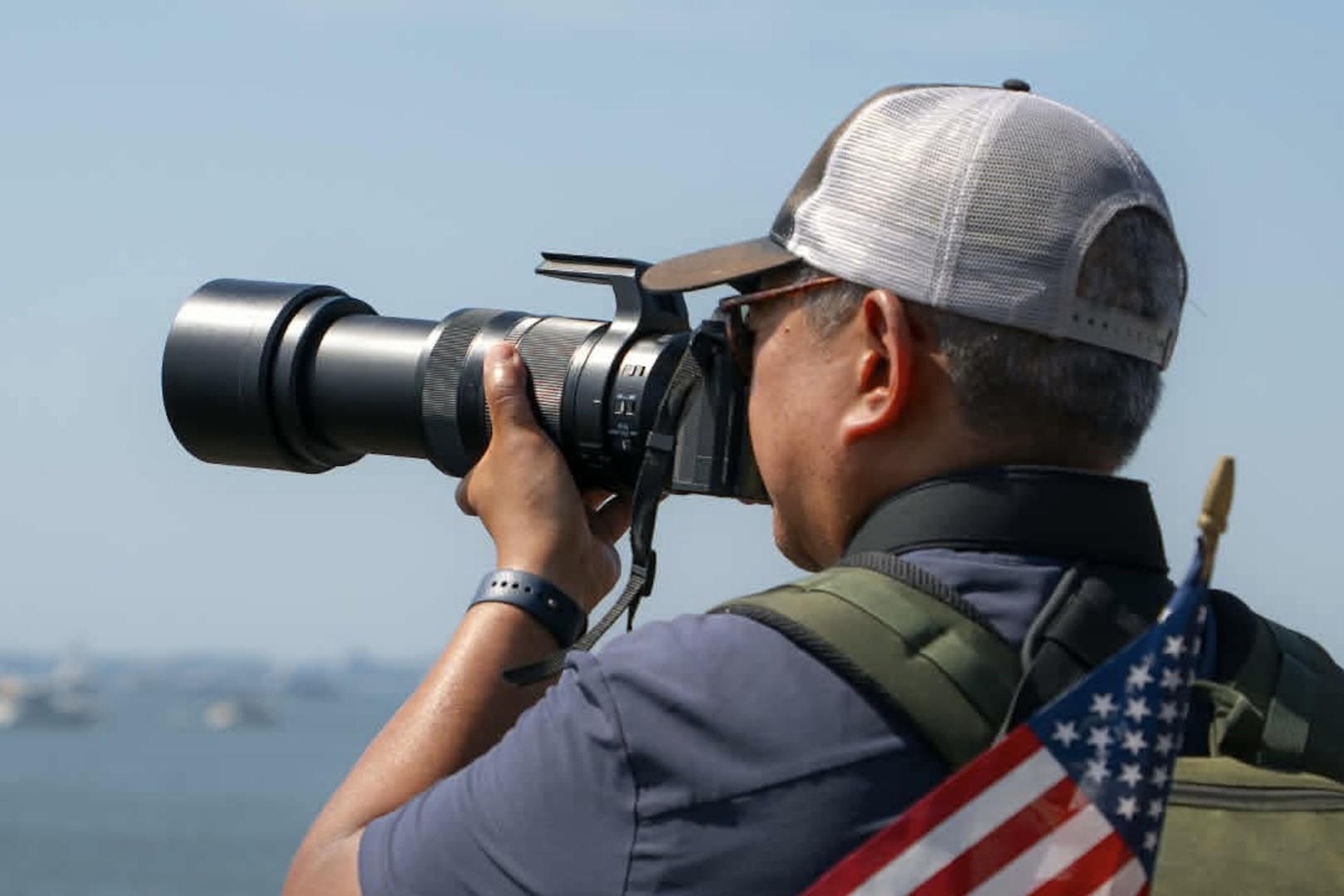 Man in cap shooting a camera with a long zoom lens.