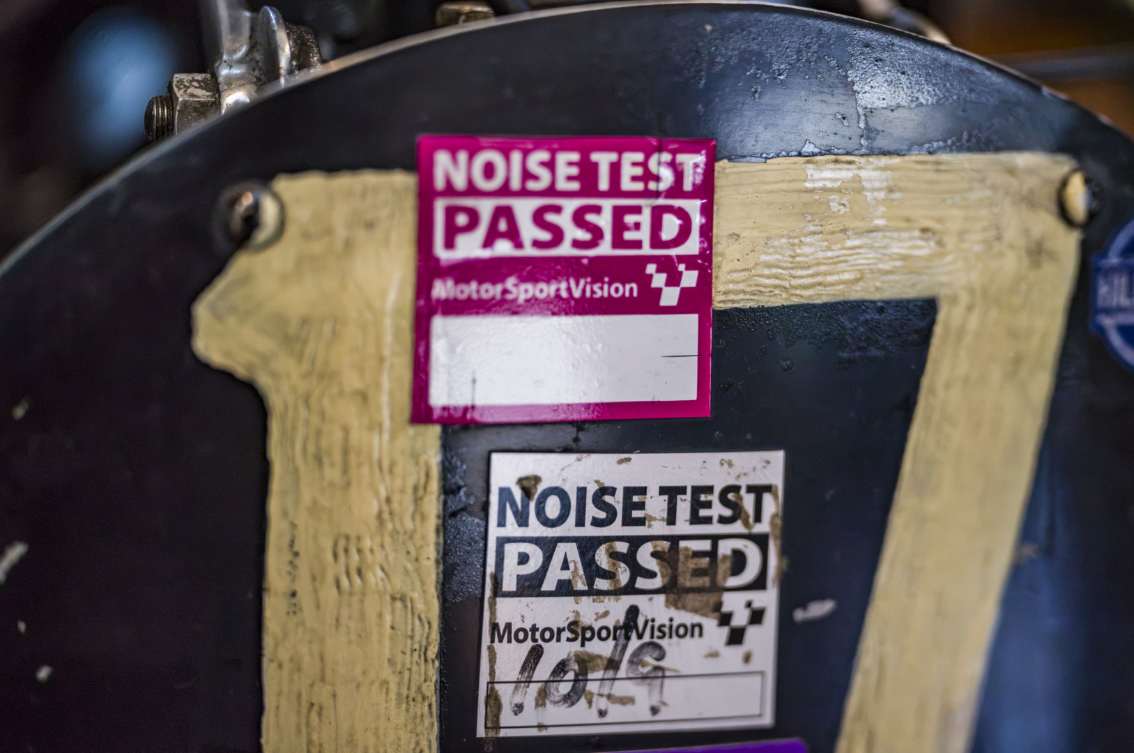 Close-up of two 'Noise Test Passed' MotorSportVision stickers on a black motorcycle number board.
