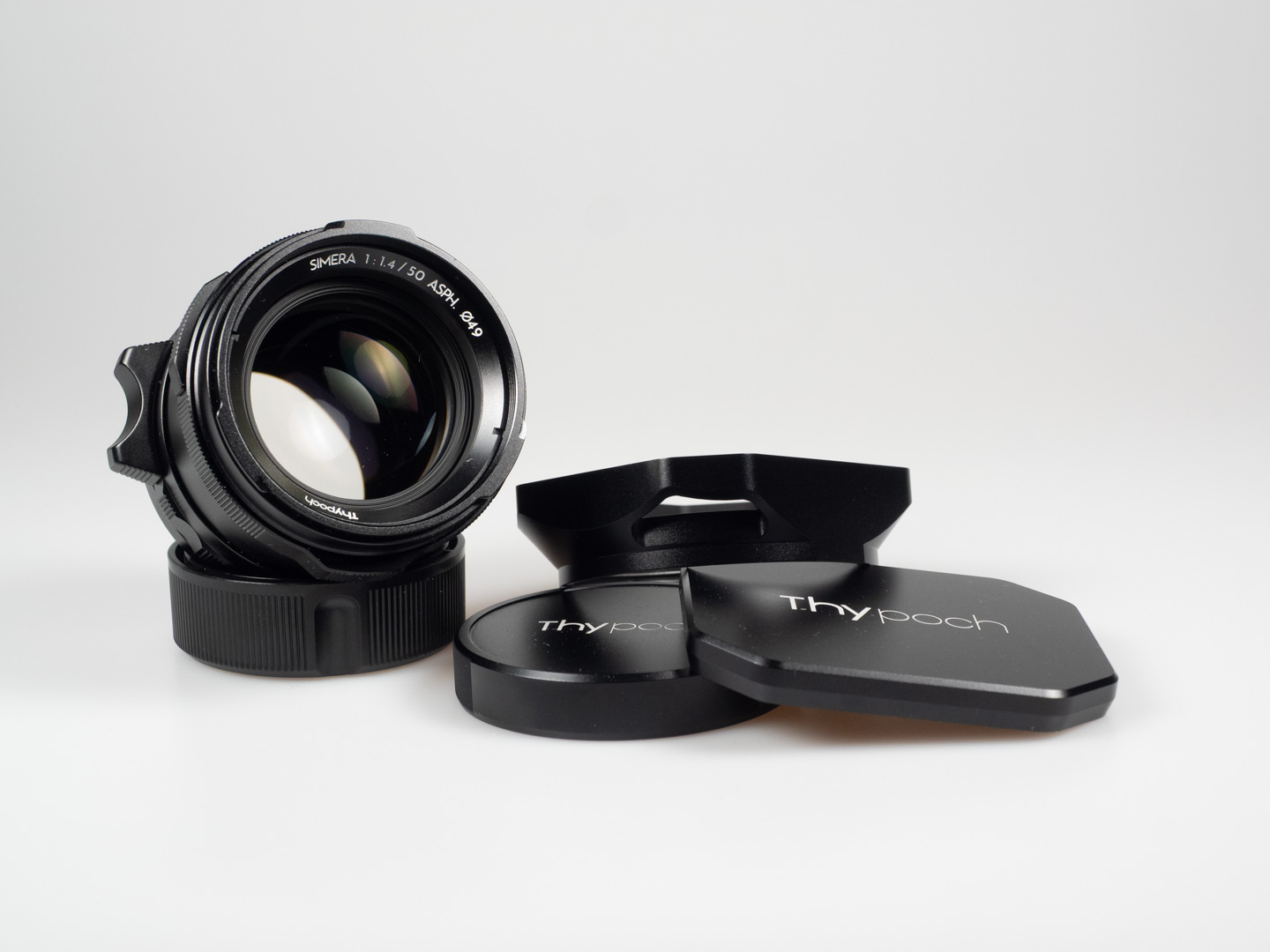 Product shot of Thypoch Simera 50/1.4: the lens beside its hood, front cap and rear cap.