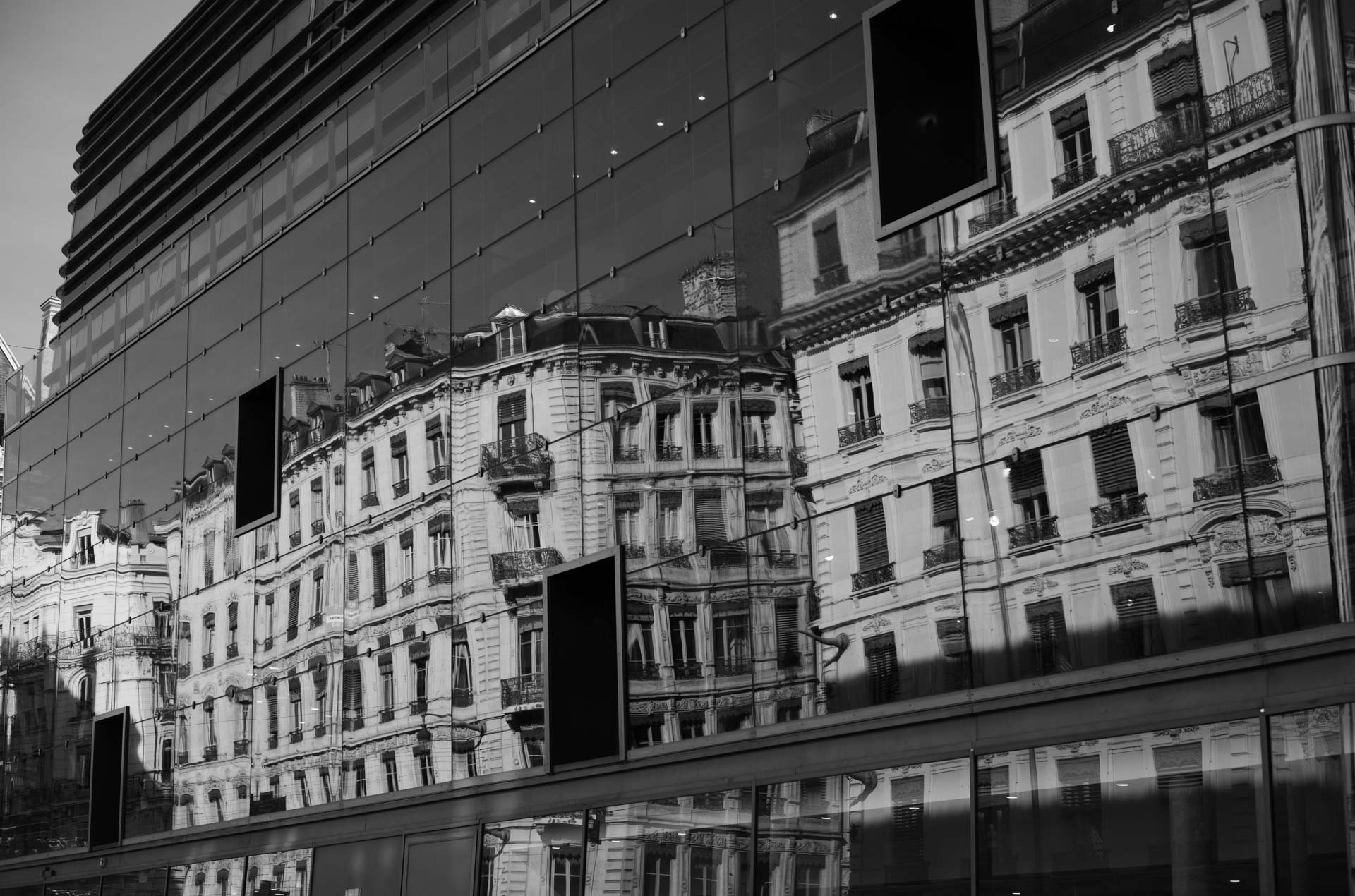 Sample shot with Thypoch Simera 50/1.4: a row of ornate 19th-century apartment buildings reflected in a modern glass facade, Lyon, France.