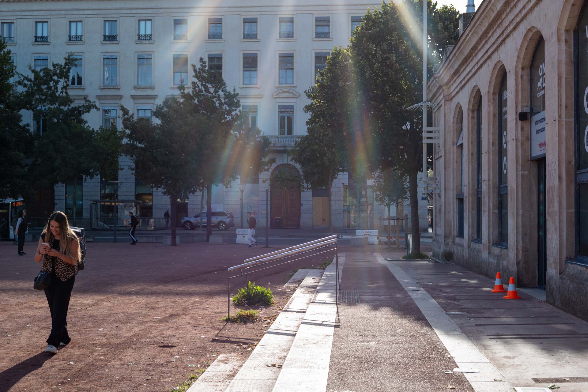 Sample shot with Thypoch Simera 50/1.4: sun rays catching a passer-by on a plaza near the Lyon tourist office at Place Bellecour, Lyon, France.