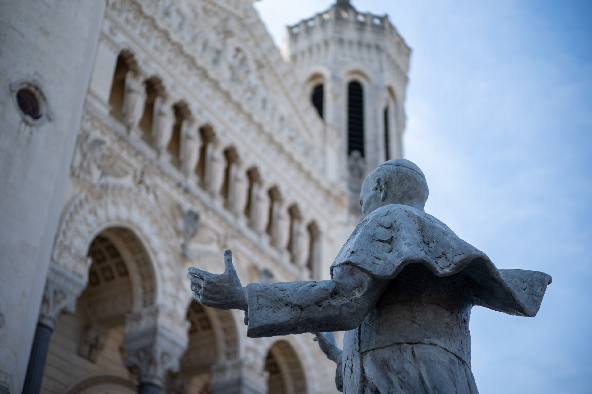 Sample shot with Thypoch Simera 50/1.4: a statue with outstretched arms before the ornate towers of the Basilique Notre-Dame de Fourvière, Lyon, France.
