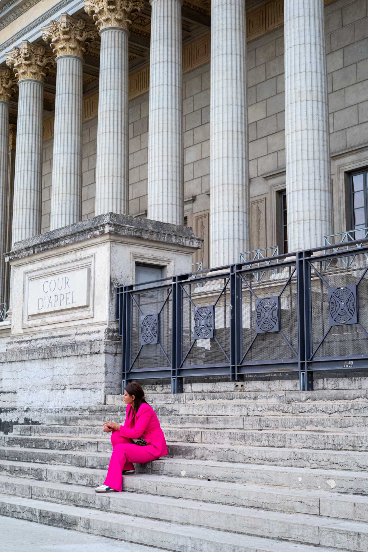 Sample shot with Thypoch Simera 50/1.4: a woman in a bright pink suit sitting on the steps of the Cour d'appel de Lyon (Palais de Justice), Lyon, France.