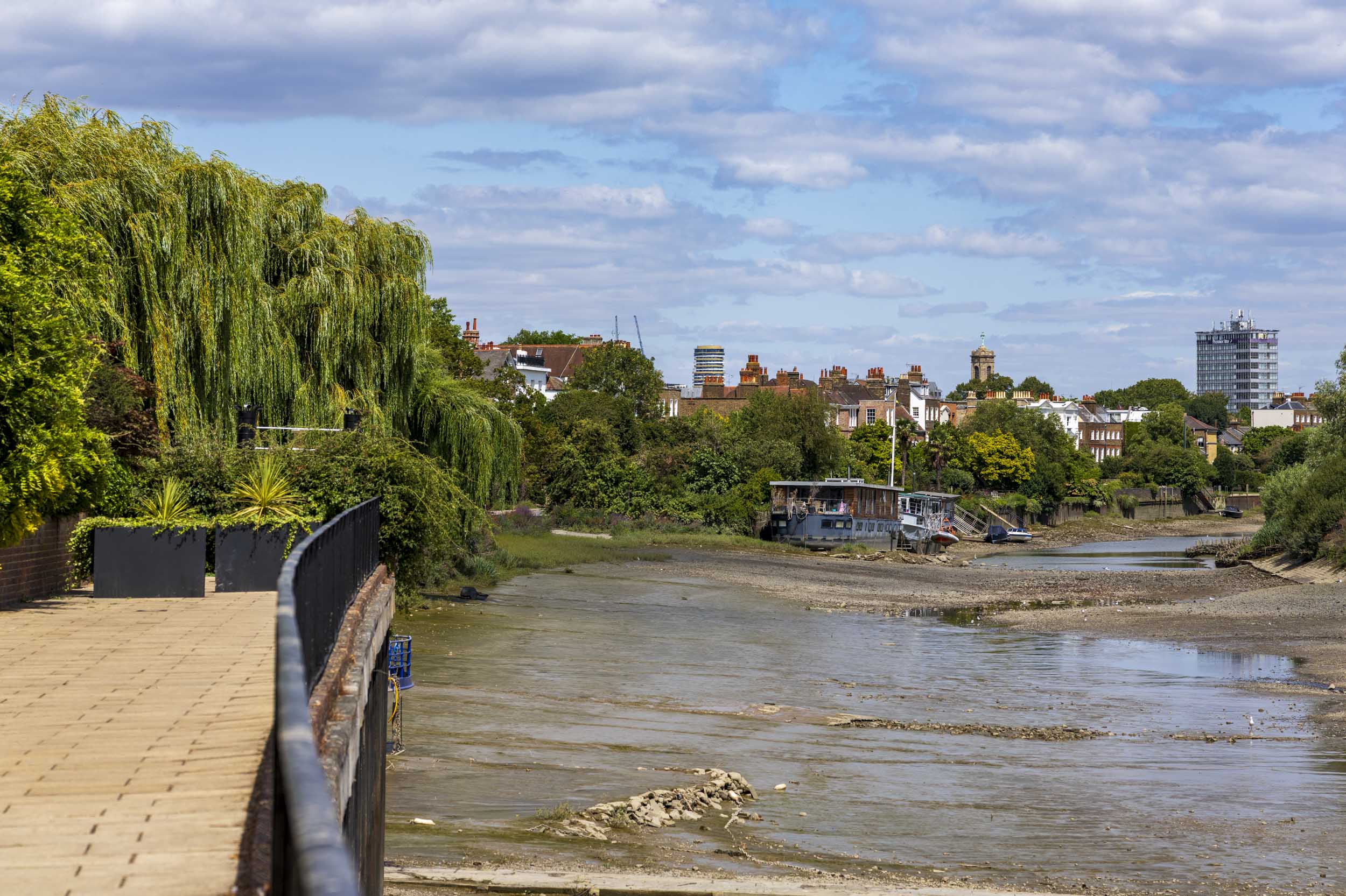 Houseboat moored on the muddy banks of the River Thames at low tide, London skyline behind