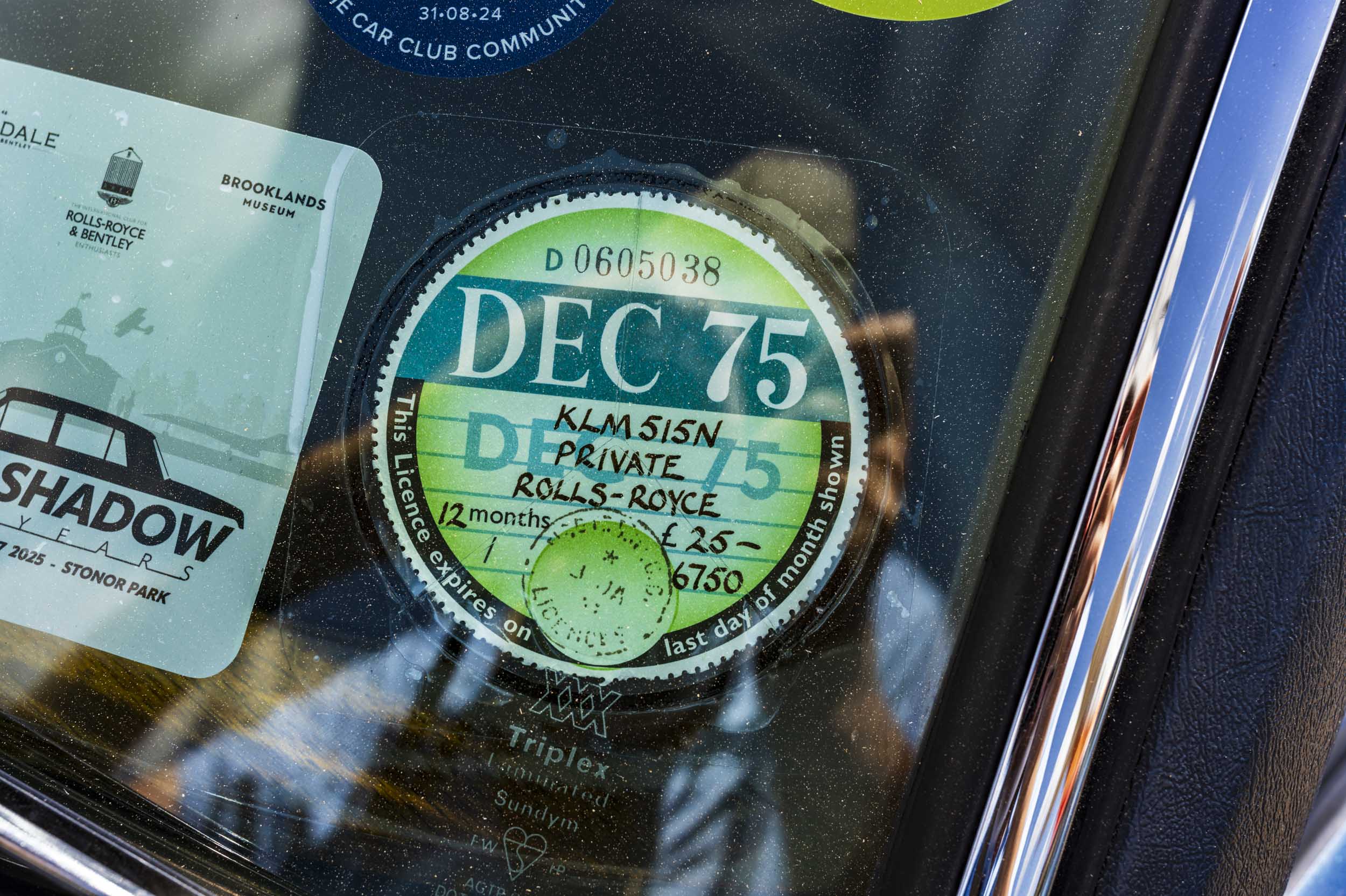 Close-up of a vintage "DEC 75" tax disc and car club stickers on a windscreen.