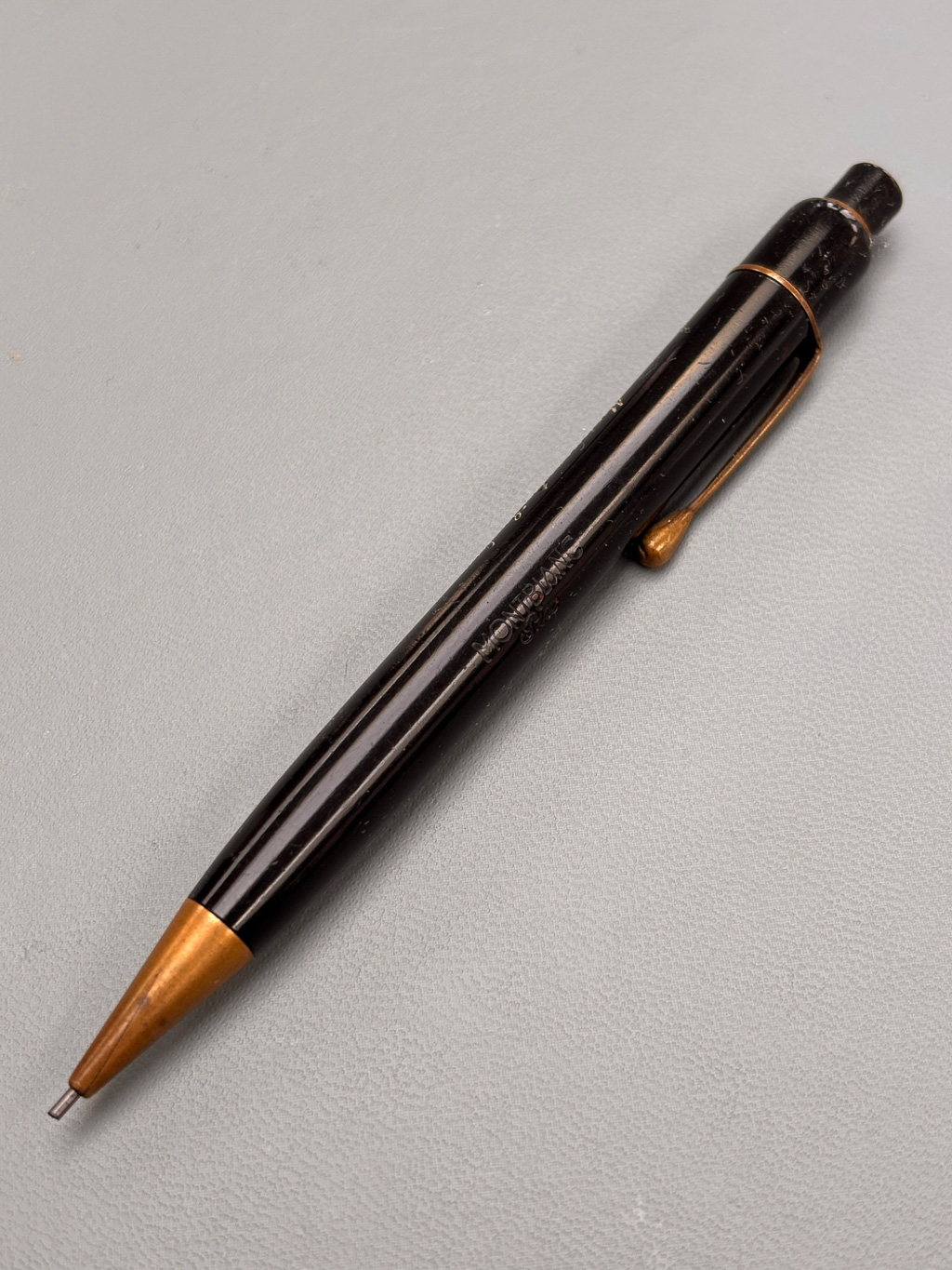 A black pen with a gold tip resting on a gray surface.