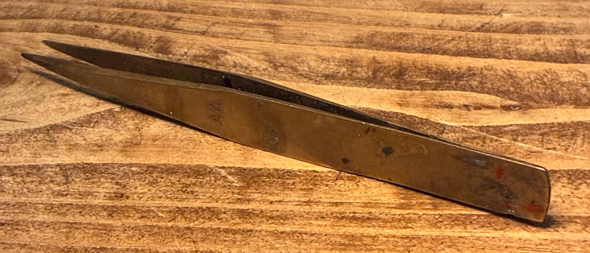A close-up image of a pair of metallic tweezers resting on a wooden surface.