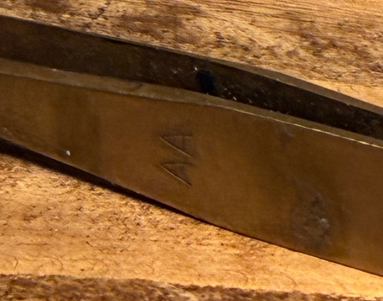 Close-up view of a metal tool with a handwritten 'NA' marking, resting on a wooden surface.