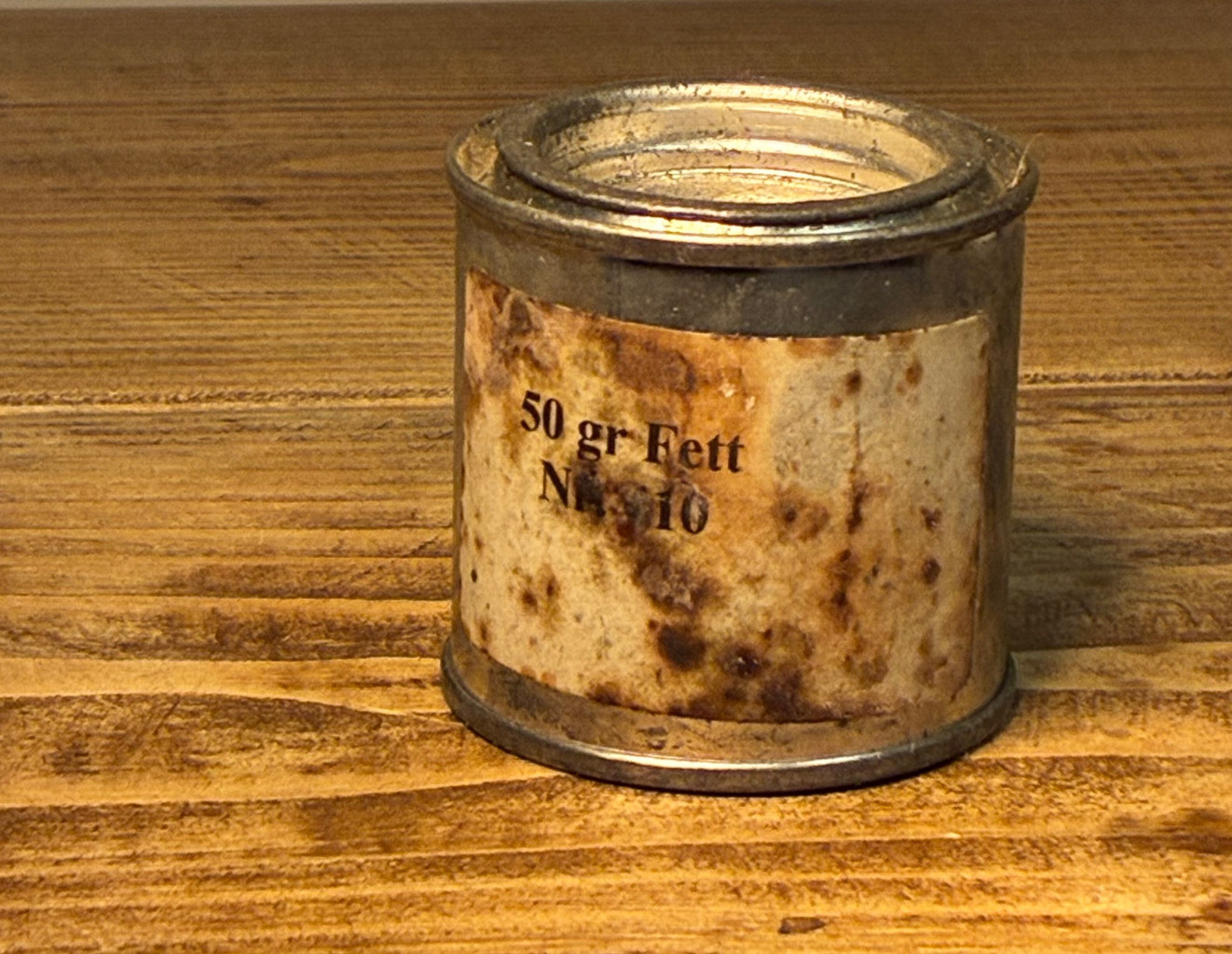 A weathered tin can labeled '50 gr Fett Nr. 10' resting on a wooden surface.
