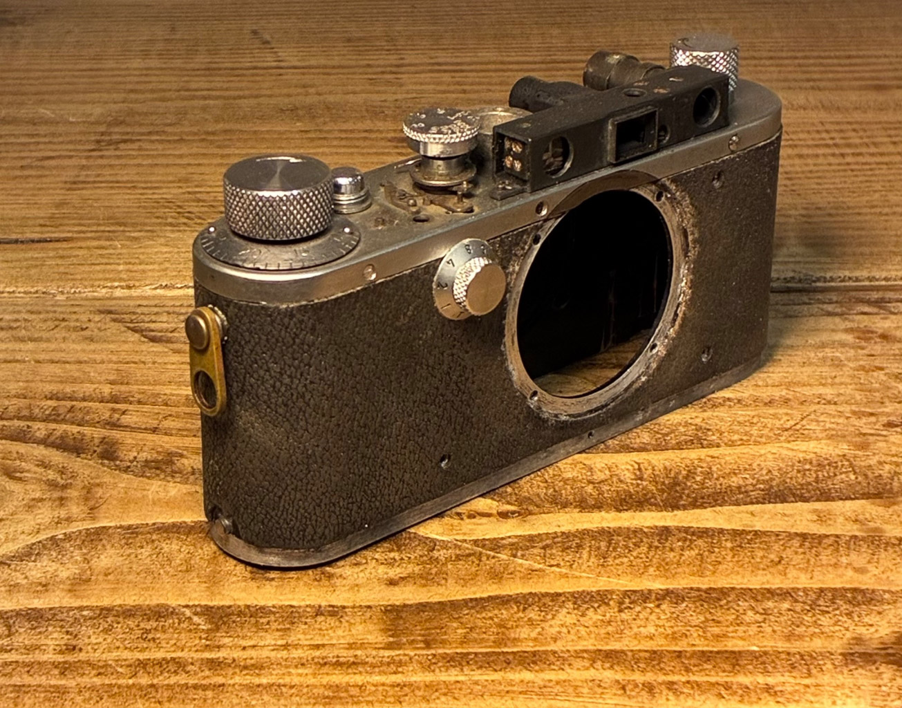 Close-up of an old, vintage camera with a leather exterior and missing lens on a wooden surface.