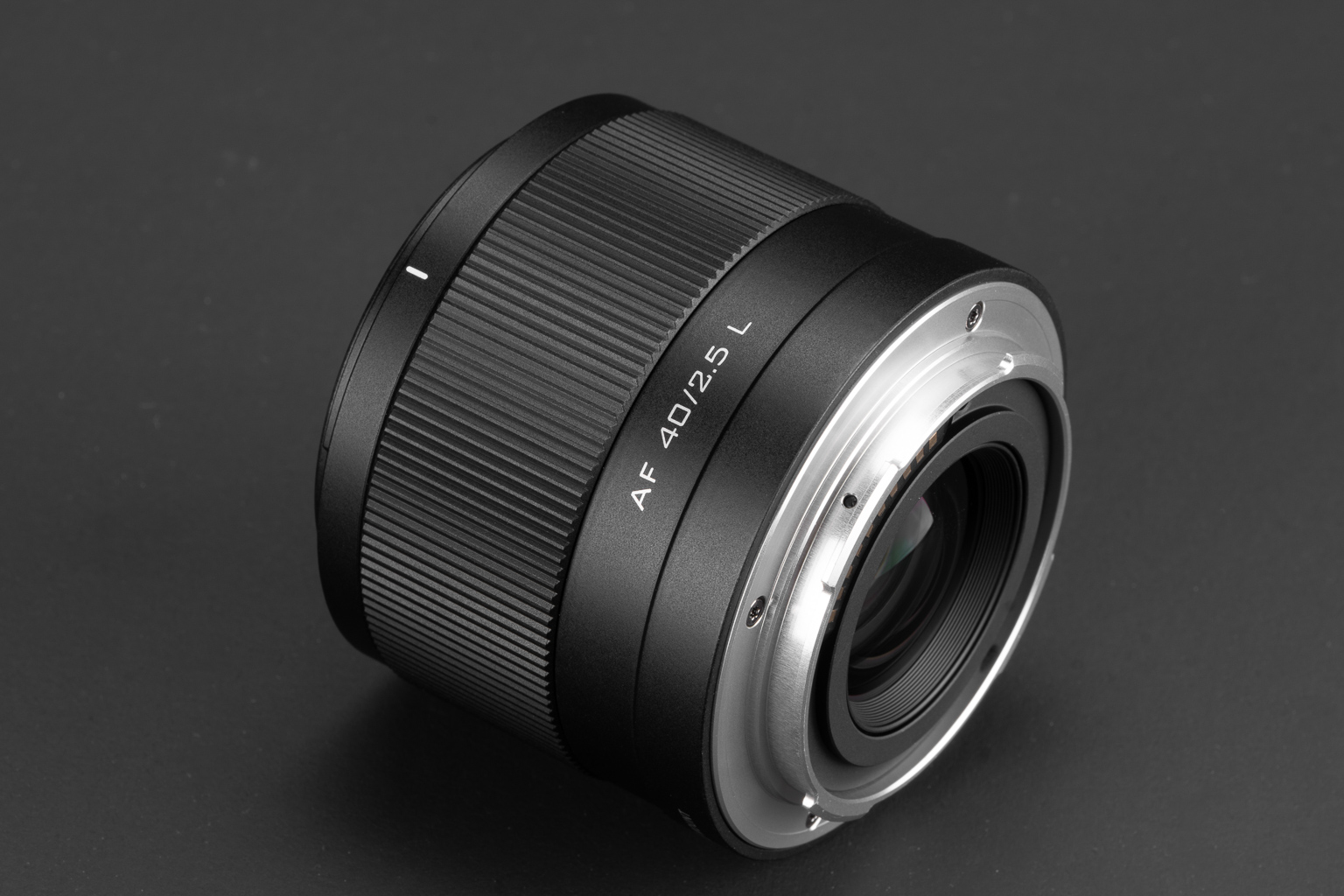 A close-up view of a black camera lens on a dark background, featuring a smooth texture and silver mounting ring.