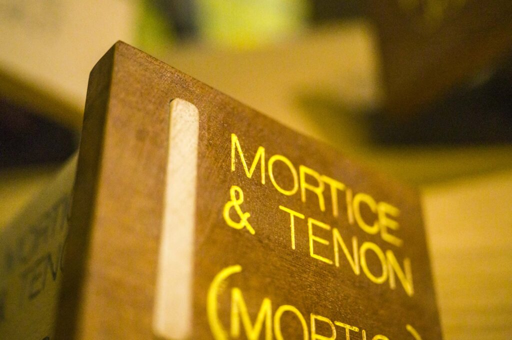 Close-up of a wooden display block engraved ‘Mortice & Tenon (Mortice)’ in yellow lettering, showing the cut mortice slot along its edge.