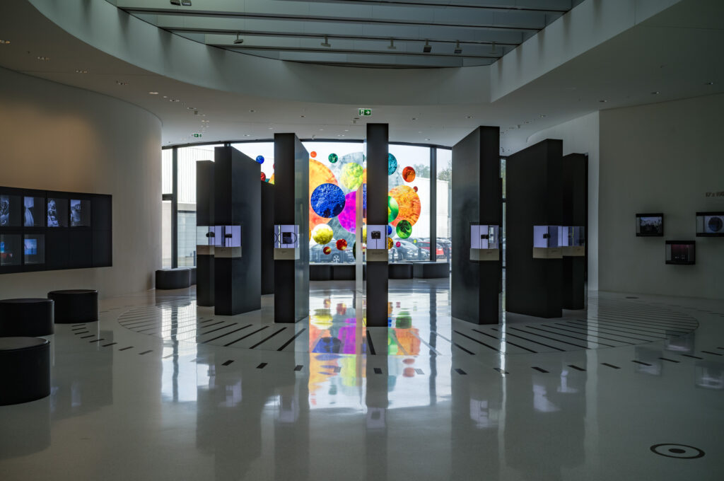 Leica Wetzlar visit: A dimly lit museum lobby with tall black display pillars and illuminated glass spheres reflected in the polished floor.