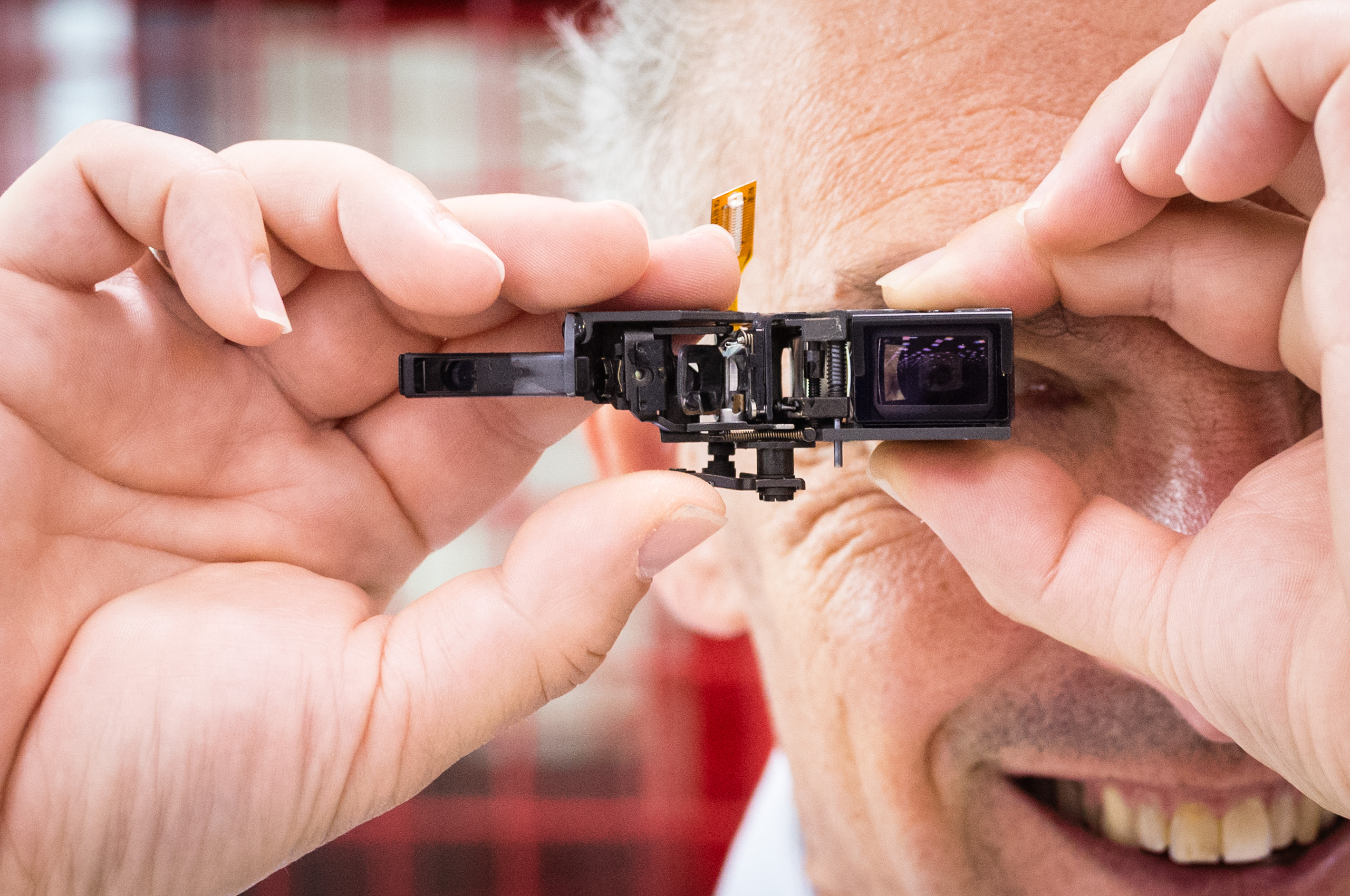 Leica Wetzlar visit: A close-up of hands holding a partially disassembled rangefinder viewfinder mechanism up to an eye for inspection.