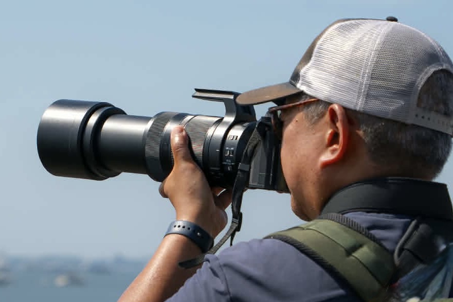 Man taking a photo with a digital mirrorless camera and telephoto zoom.