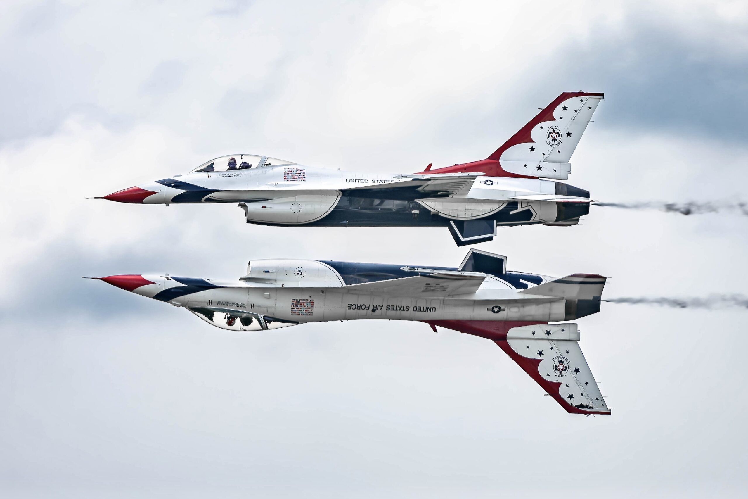 Two Thunderbirds F-16s flying in mirrored formation, one upright and one inverted, both trailing smoke.