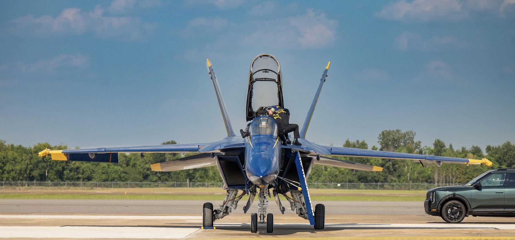 A head-on view of a Blue Angels F/A-18 on the runway as ground crew climb over the cockpit.
