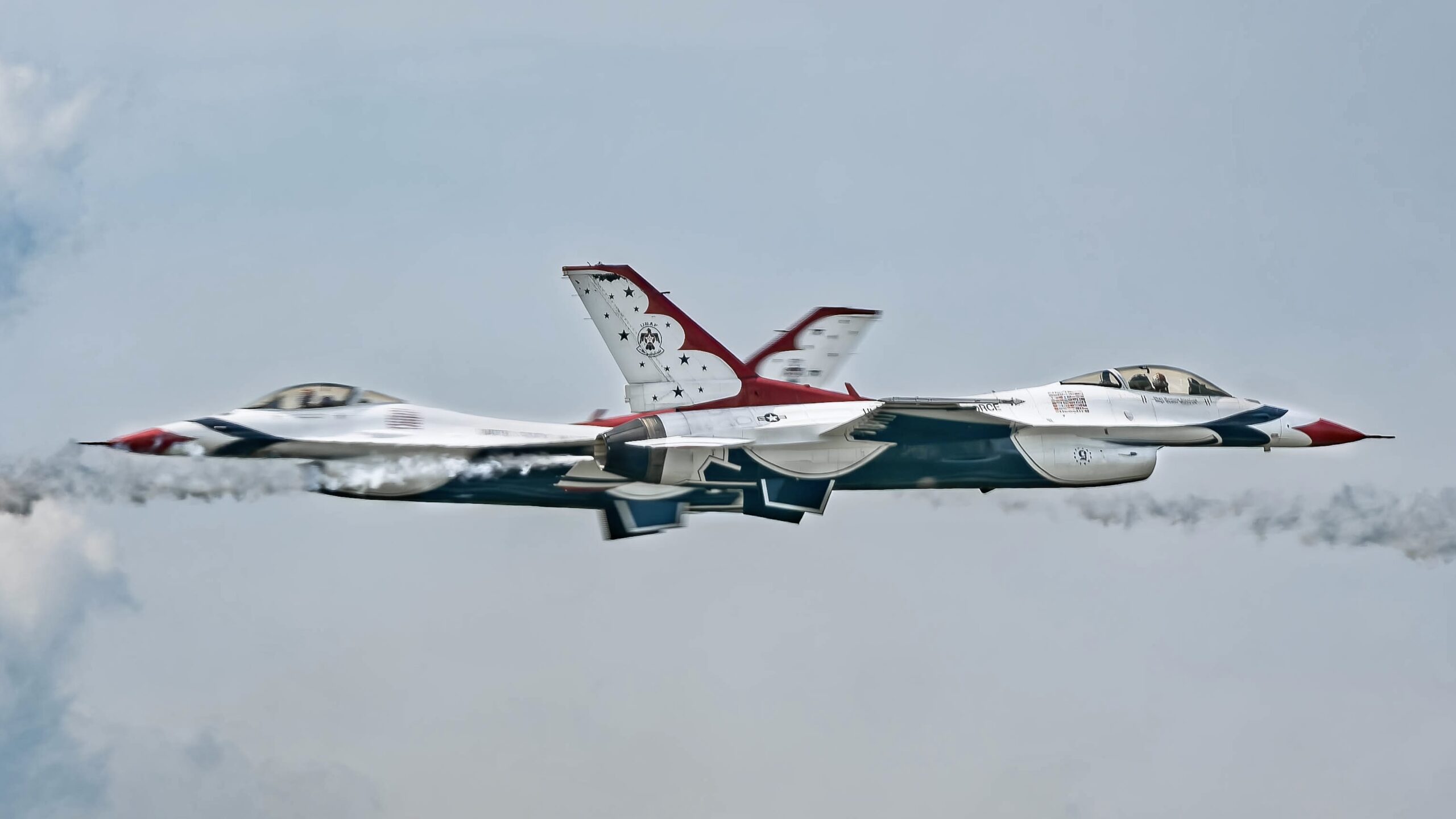 Two Thunderbirds F-16s crossing paths in opposite directions against a pale sky.