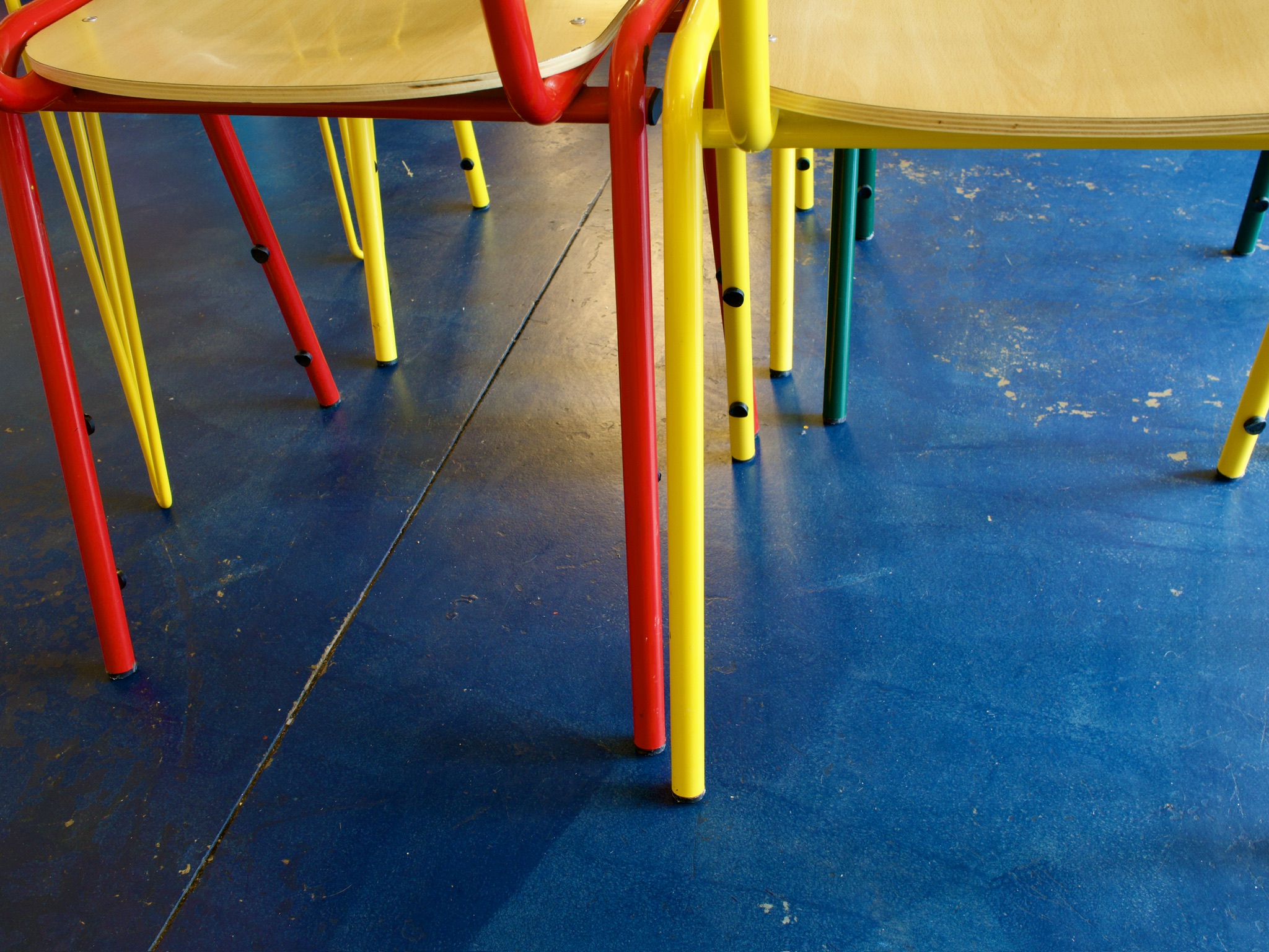 Close-up of red, yellow and green tubular chair legs on a scuffed blue floor.