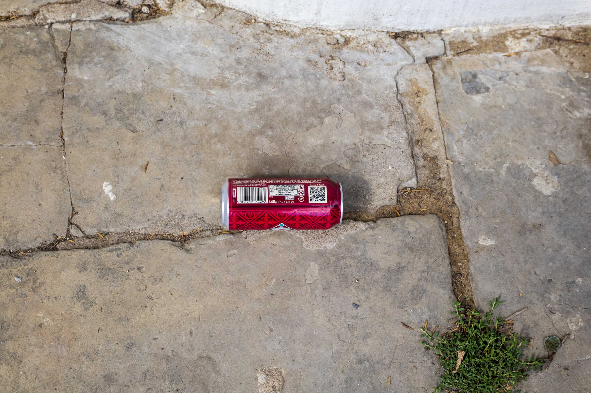 A discarded red drinks can lies on cracked paving slabs.