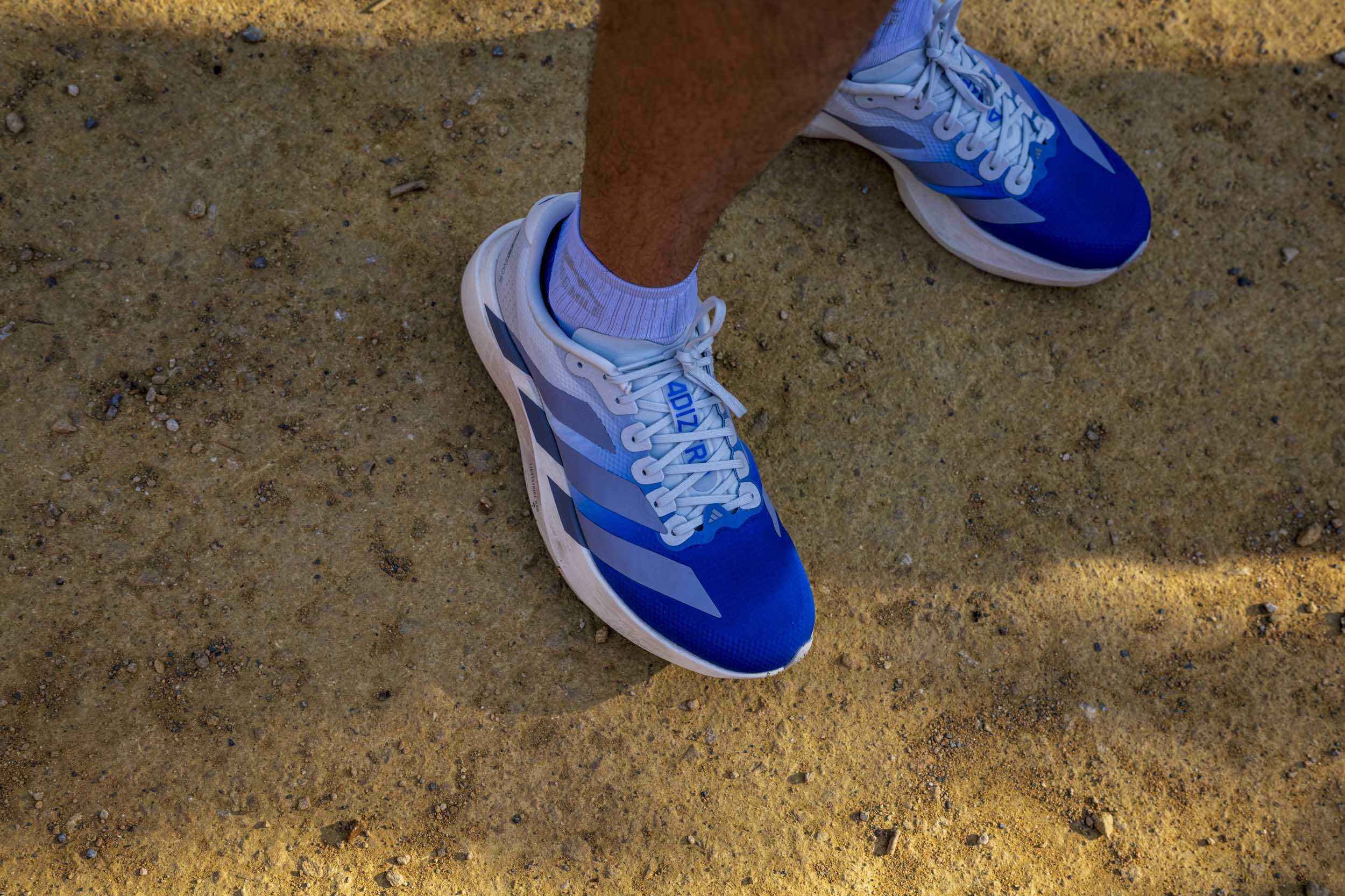 A close-up of a runner's feet in blue and white trainers, standing on a gravel path.