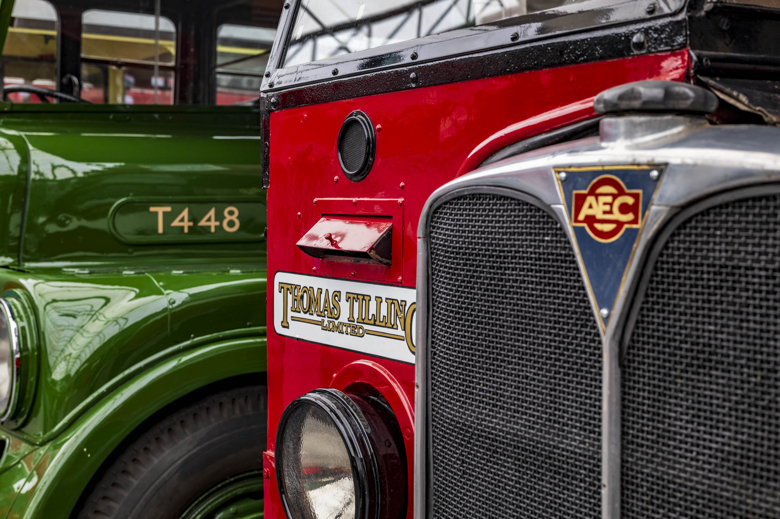 The fronts of two vintage buses side by side — a red AEC bus in Thomas Tilling livery and a green bus numbered T448.