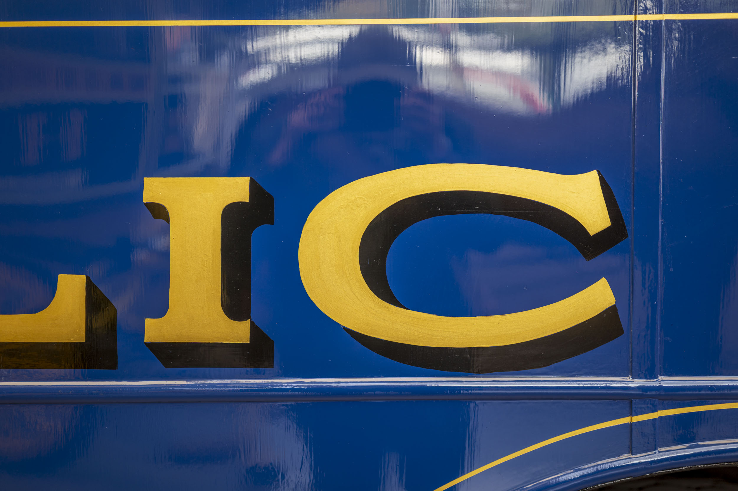 Gold sign-writer's lettering reading '...LIC' on glossy blue enamel, continuing from an earlier frame on the same vehicle.