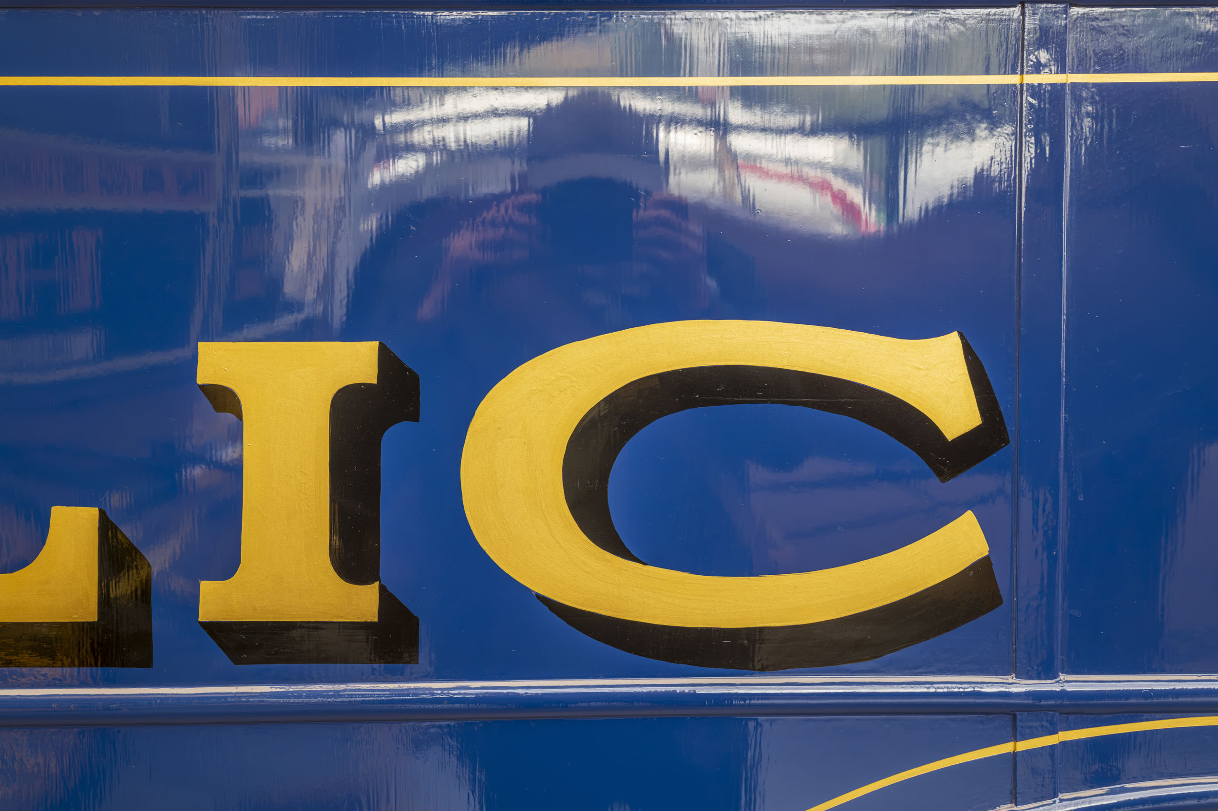 Gold sign-writer's lettering on glossy blue enamel, part of an extended aperture test series.