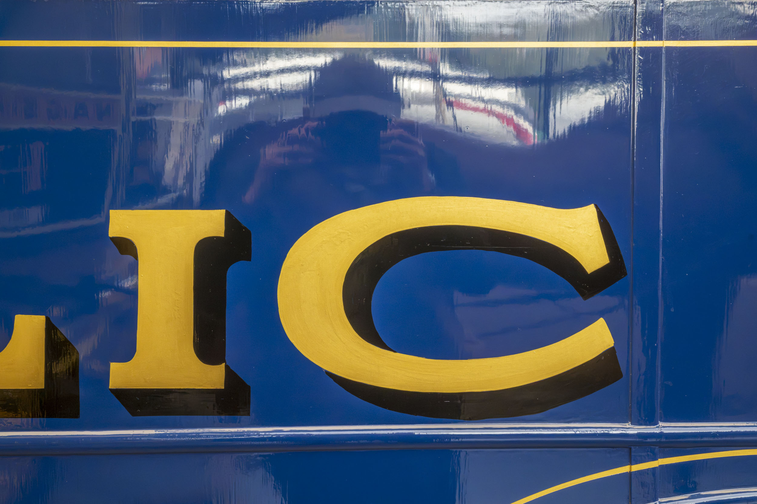 Gold sign-writer's lettering on glossy blue enamel, part of an extended aperture test series.