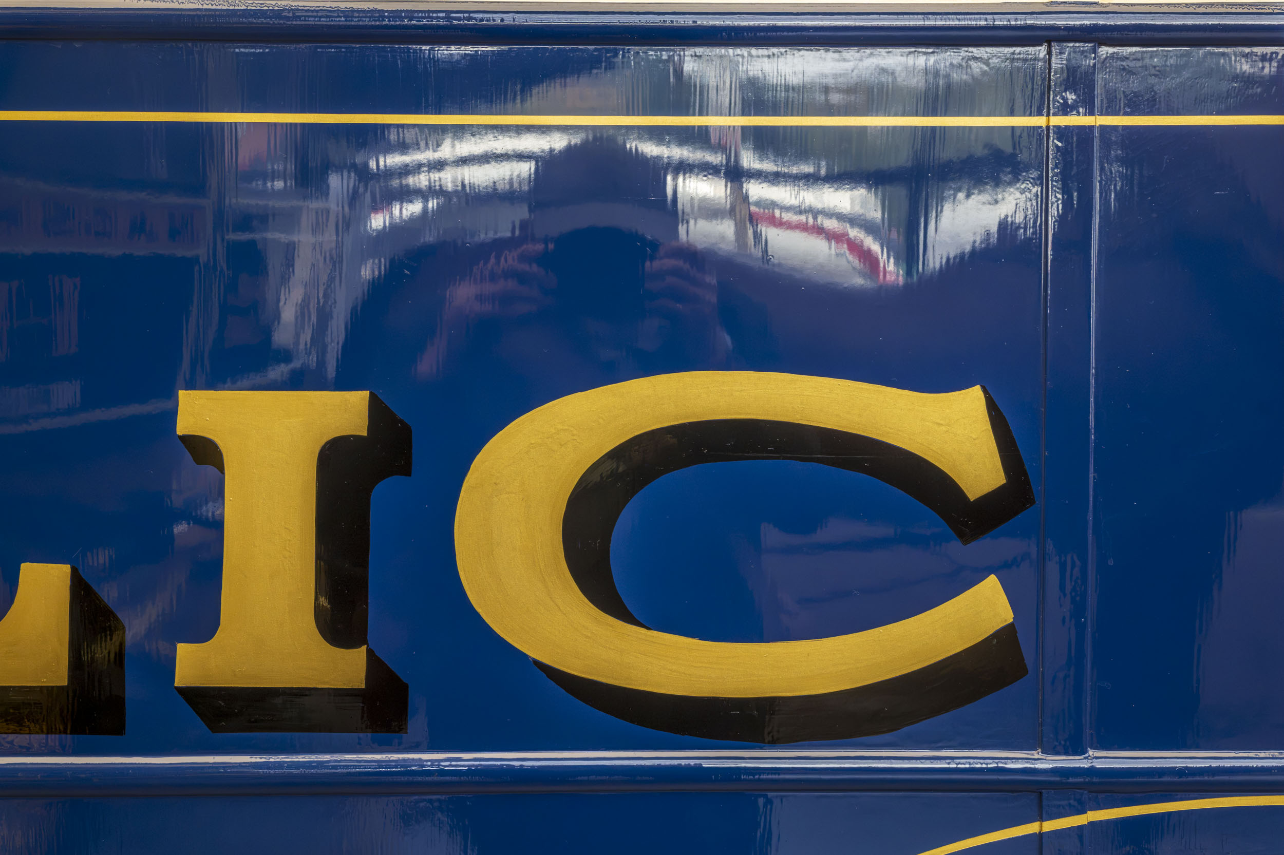 Gold sign-writer's lettering on glossy blue enamel, part of an extended aperture test series.
