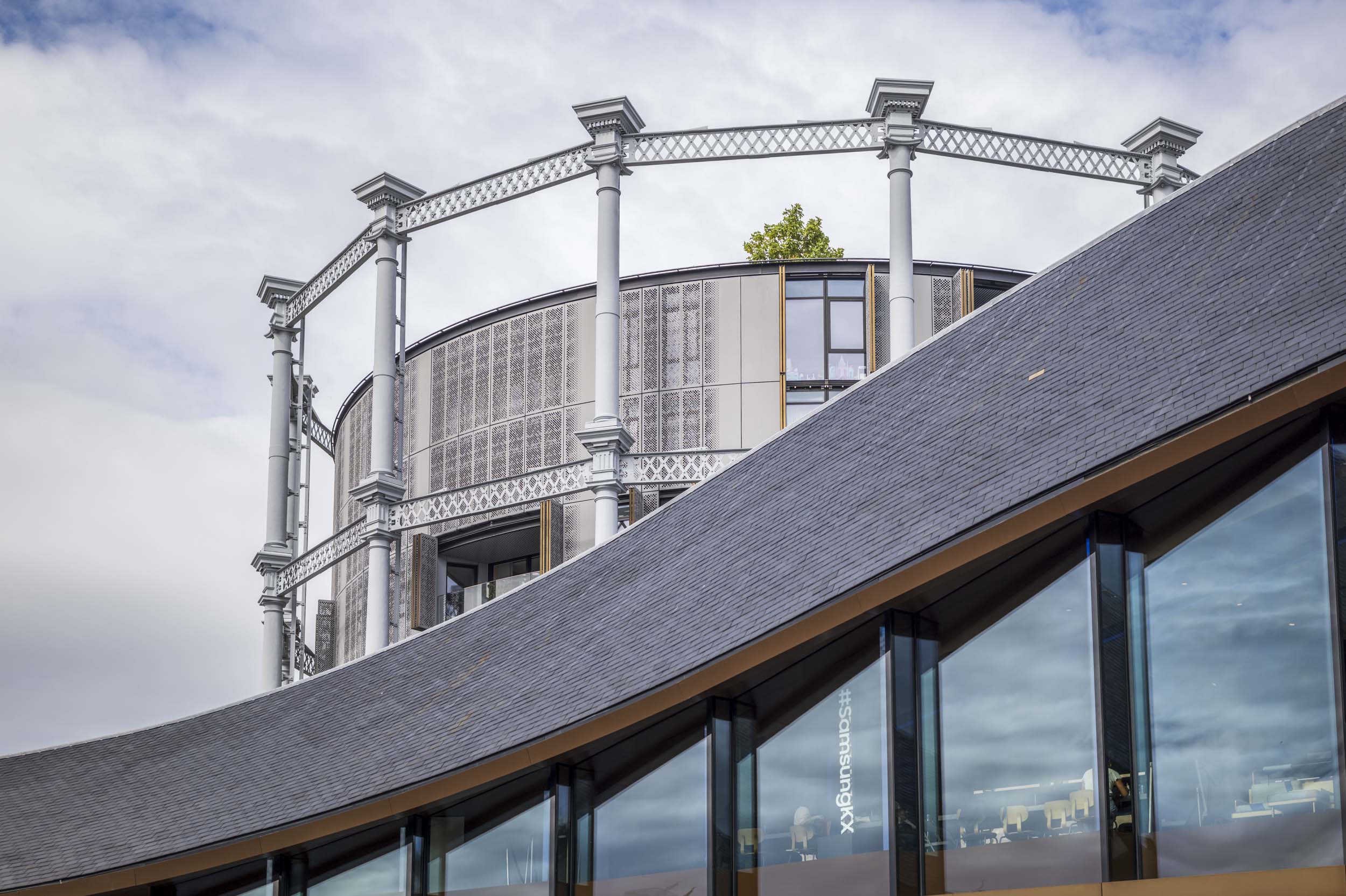The restored Victorian gasholder frame apartments rising behind the curved slate roof of the Samsung KX building at King's Cross.