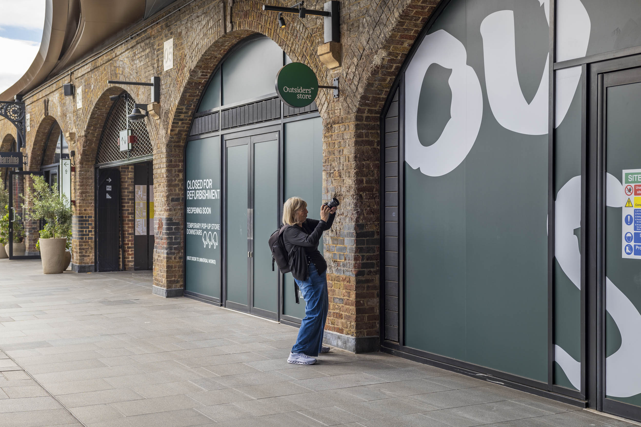 A woman photographs a row of converted railway-arch shopfronts at Coal Drops Yard, King's Cross.