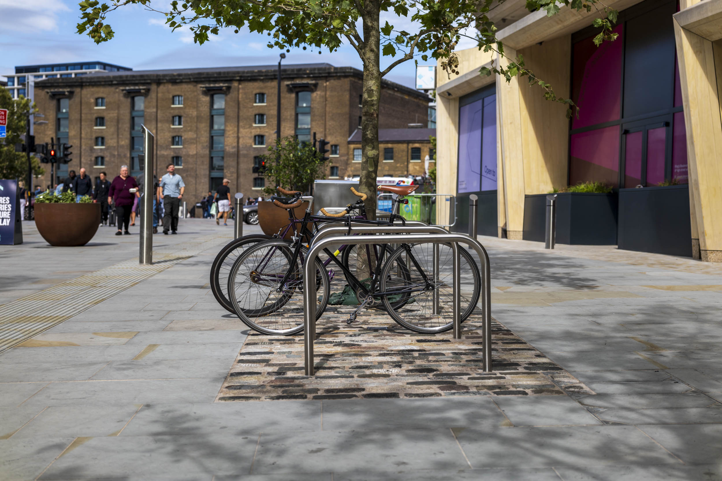 Bicycles locked to a steel rack on a cobbled patch of pavement, with a Victorian warehouse building behind.