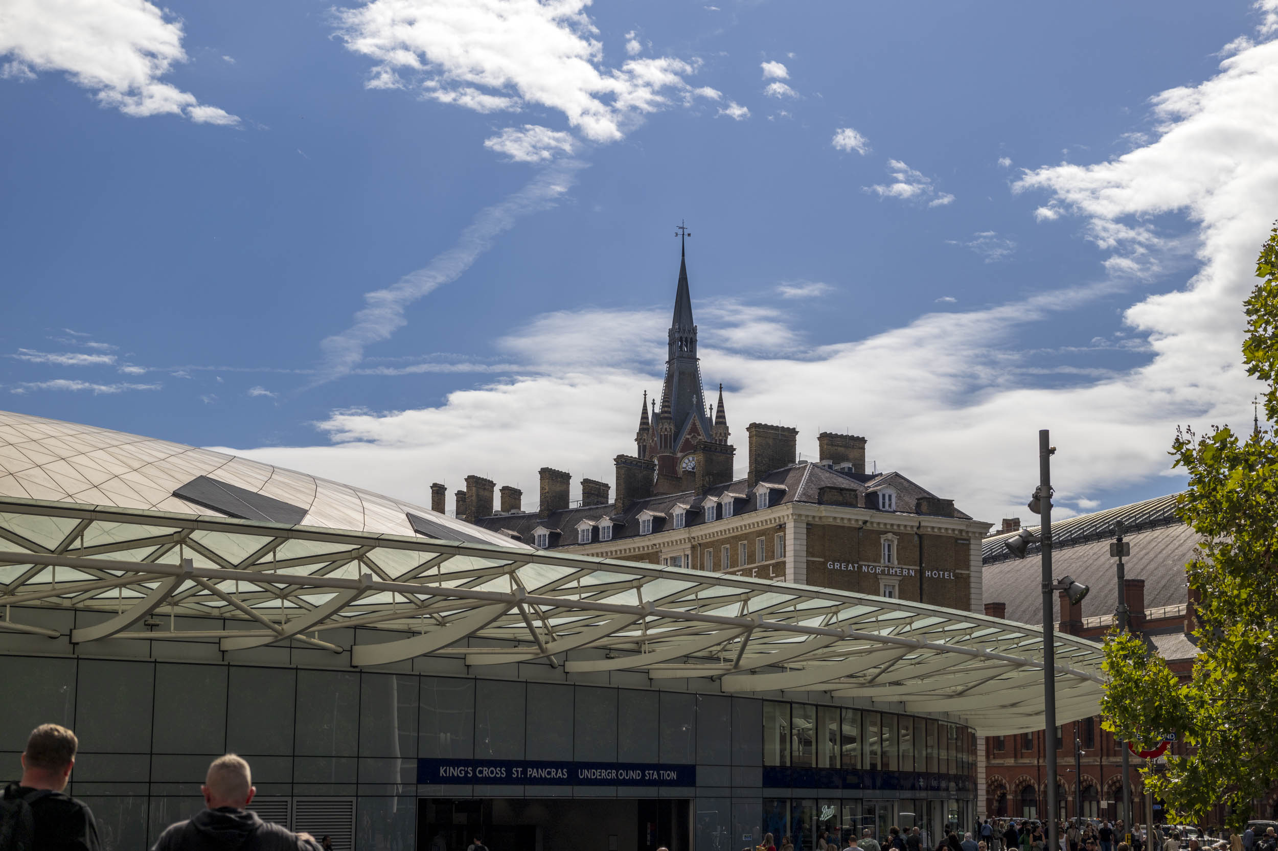 The modern canopy roof of King's Cross St Pancras Underground station, with the Gothic spire of the Great Northern Hotel behind.