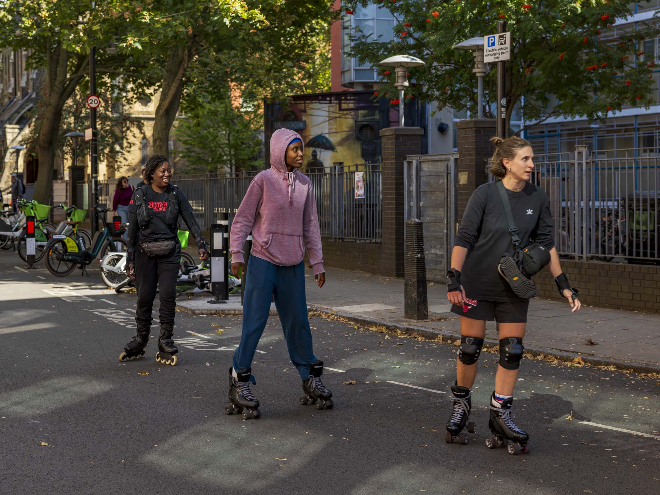 Three rollerbladers skate along a tree-lined London street on a sunny autumn day.