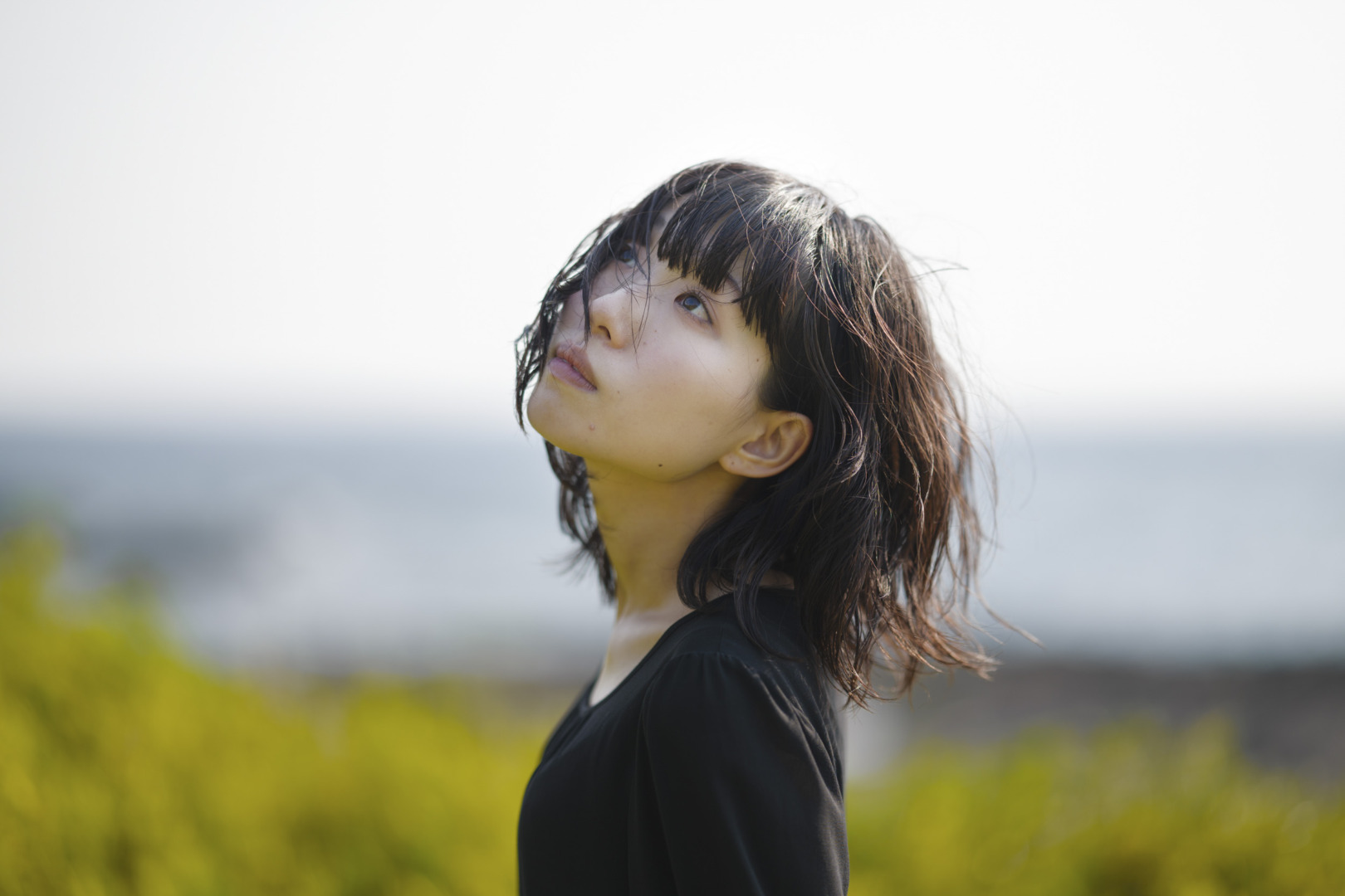 A young woman with windswept hair looking upward against a bright sky.