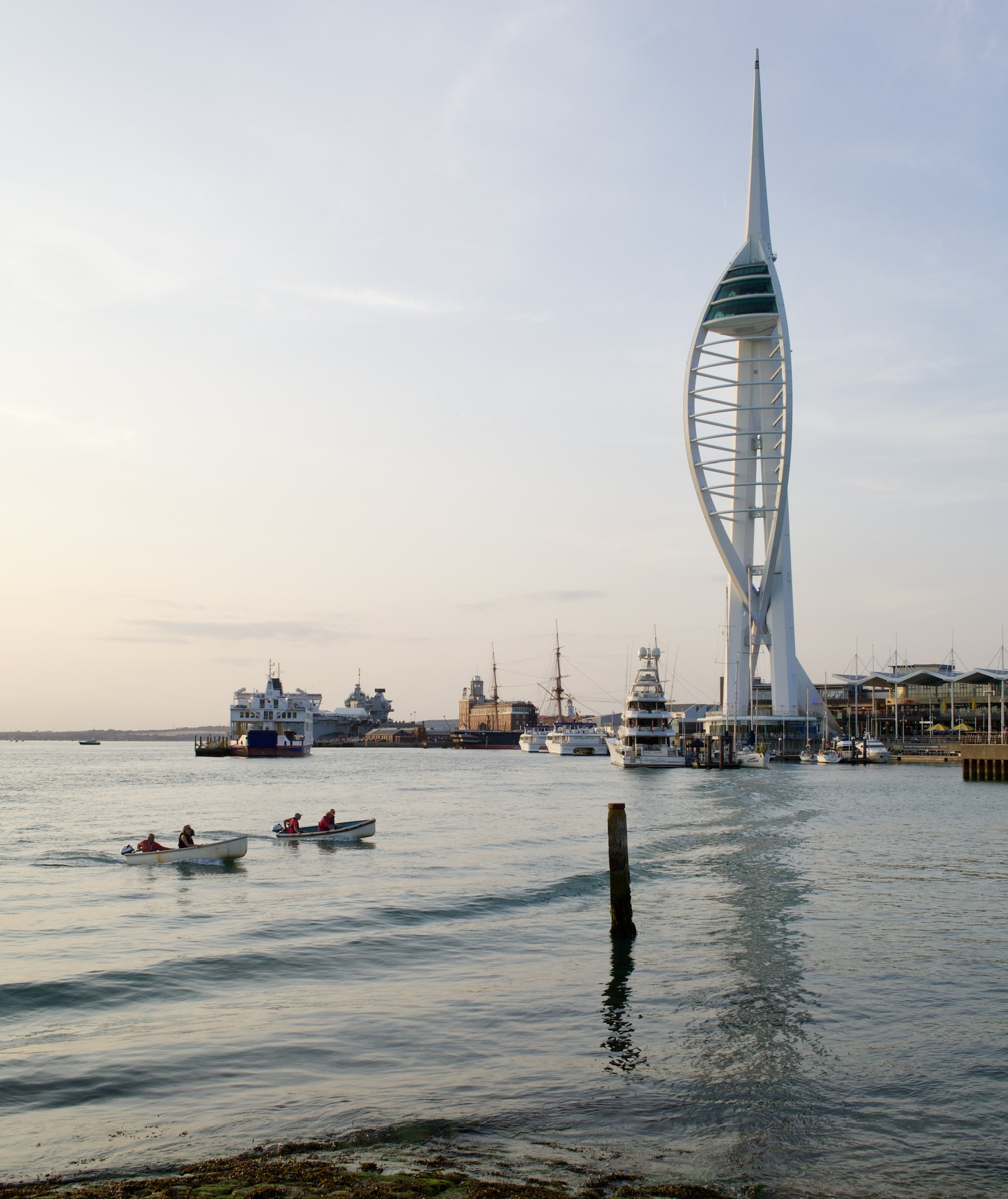 Two small motorboats pass in front of Portsmouth's Spinnaker Tower and harbour at dusk.