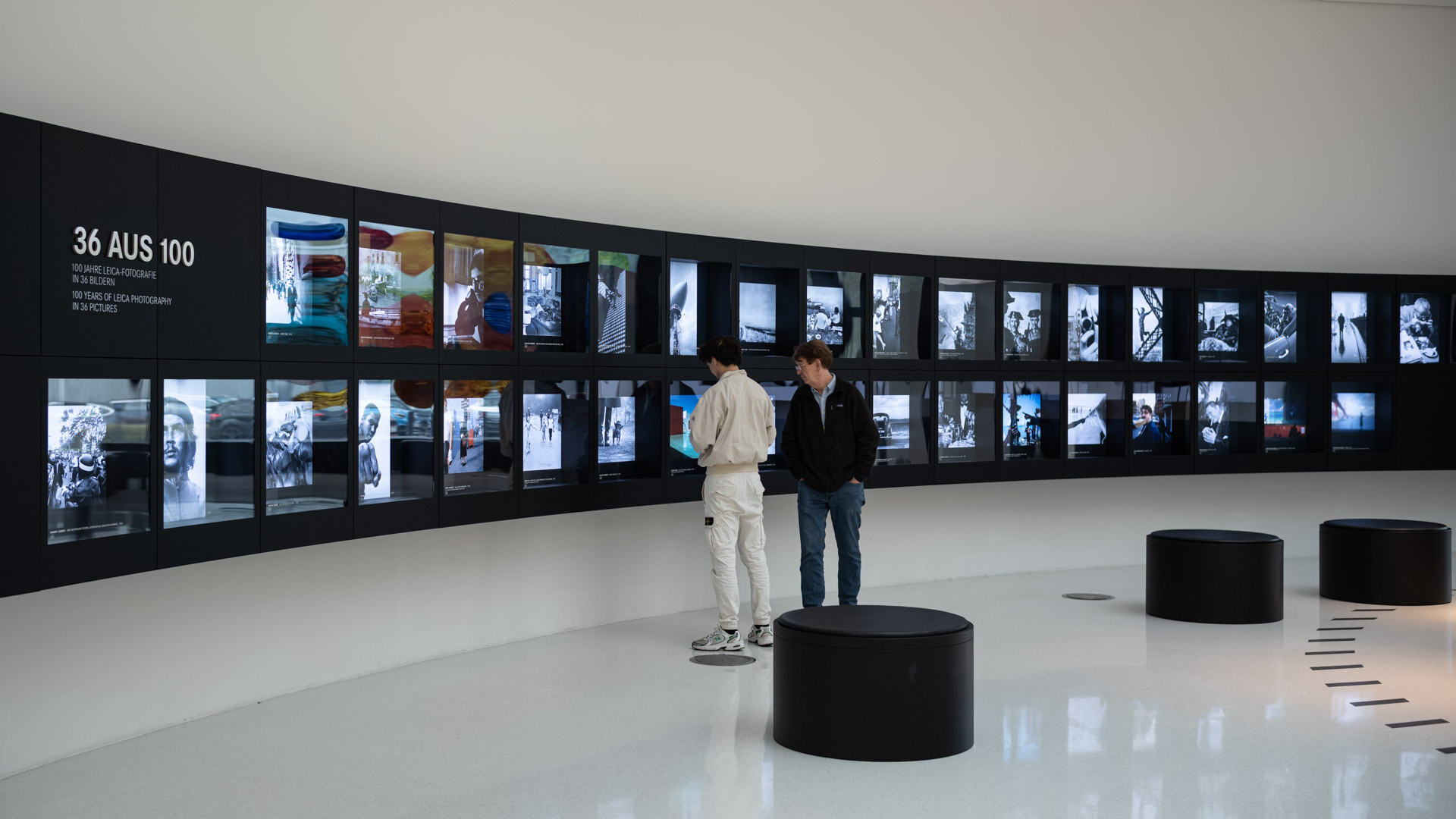 Leica Wetzlar visit: Two visitors viewing the '36 aus 100' wall of screens showing highlights from a century of Leica photography.