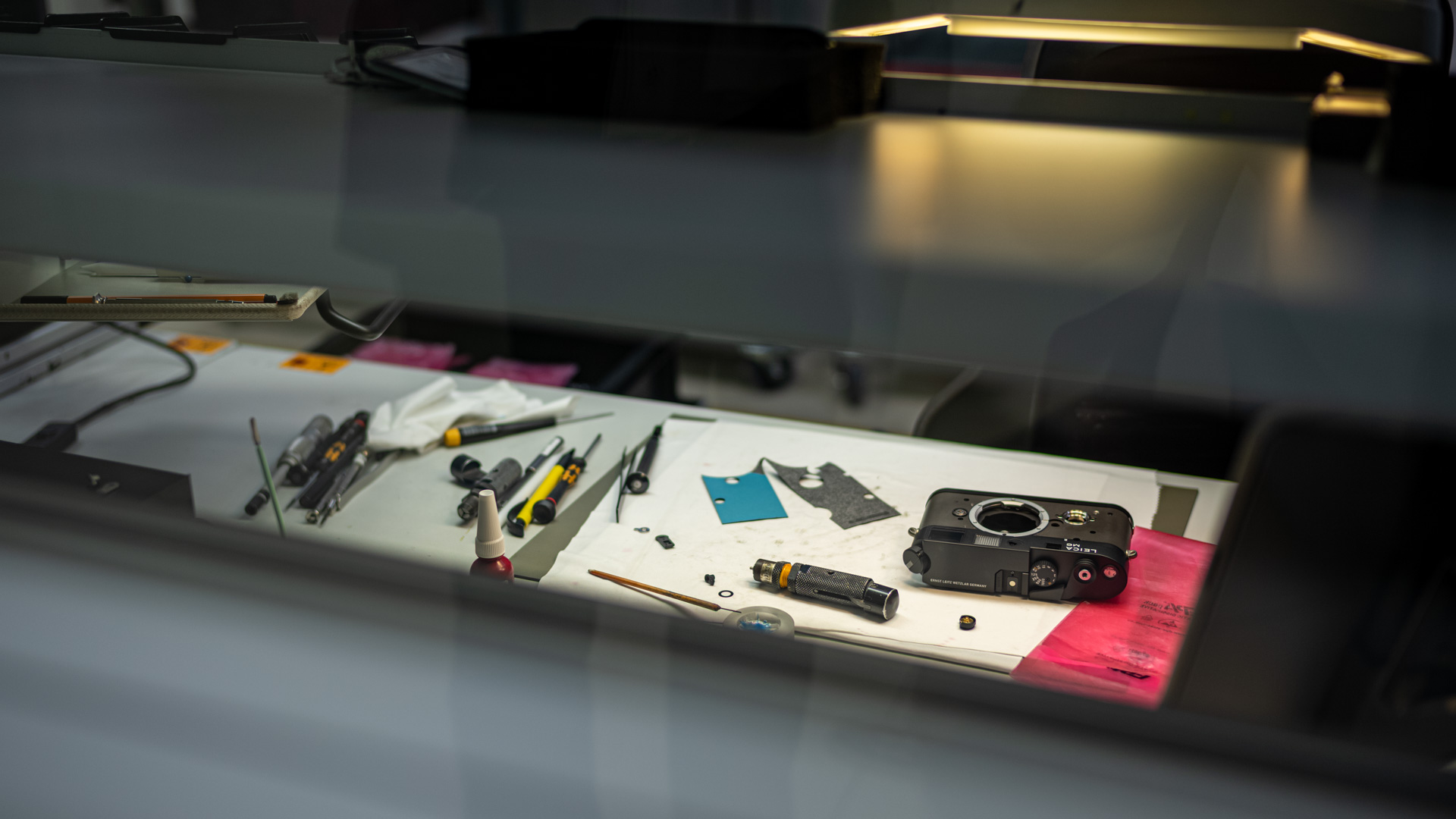 Leica Wetzlar visit: A reflected view through glass of a manufacturing bench holding screwdrivers, tools, and a partially disassembled Leica M camera body.