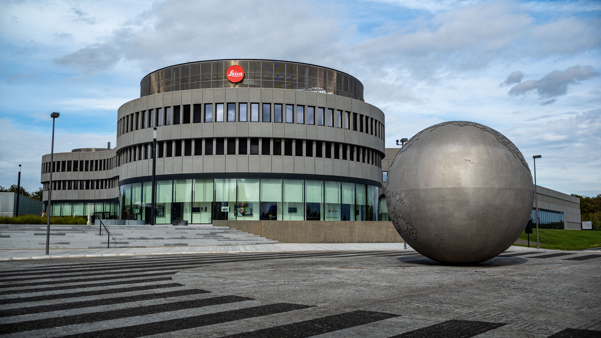 Leica Wetzlar visit: The round Leica Camera headquarters building with a large sculpted metal sphere in the square in front of it.