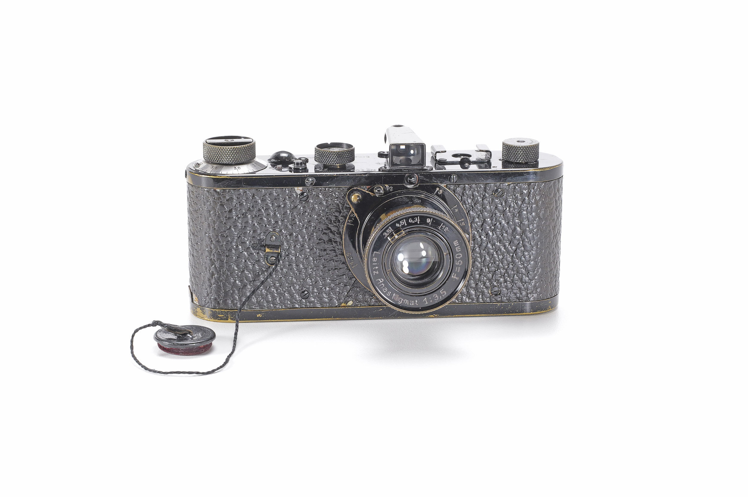 A worn black Leica 0-Series camera with a collapsible 50mm lens and a lens cap on a cord, photographed from the front on a white background.